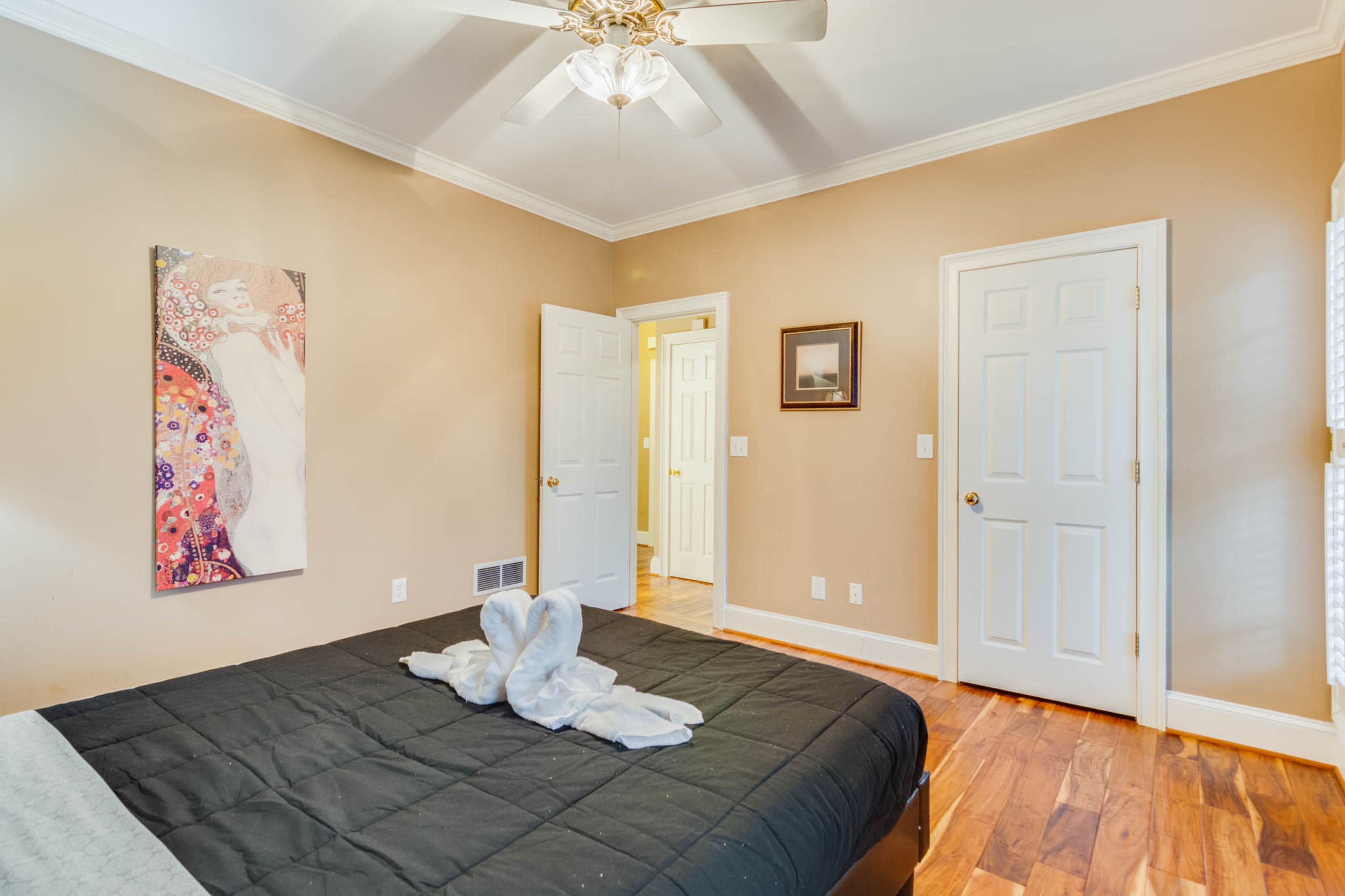 The image shows a bedroom with a black bedspread, a decorative wall painting, and double doors leading to another room.