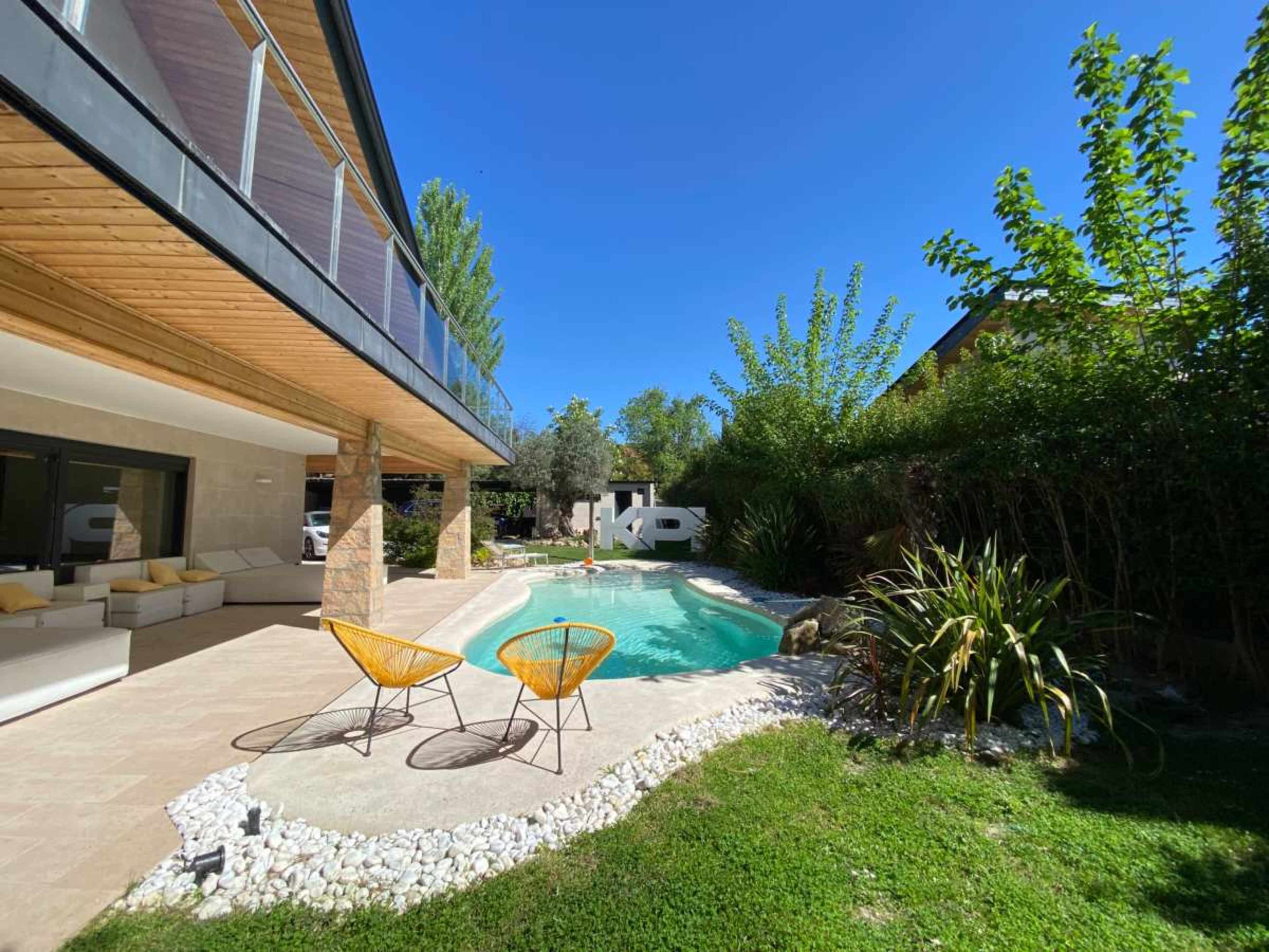 A modern home features a landscaped yard with a swimming pool surrounded by lounging chairs and greenery.