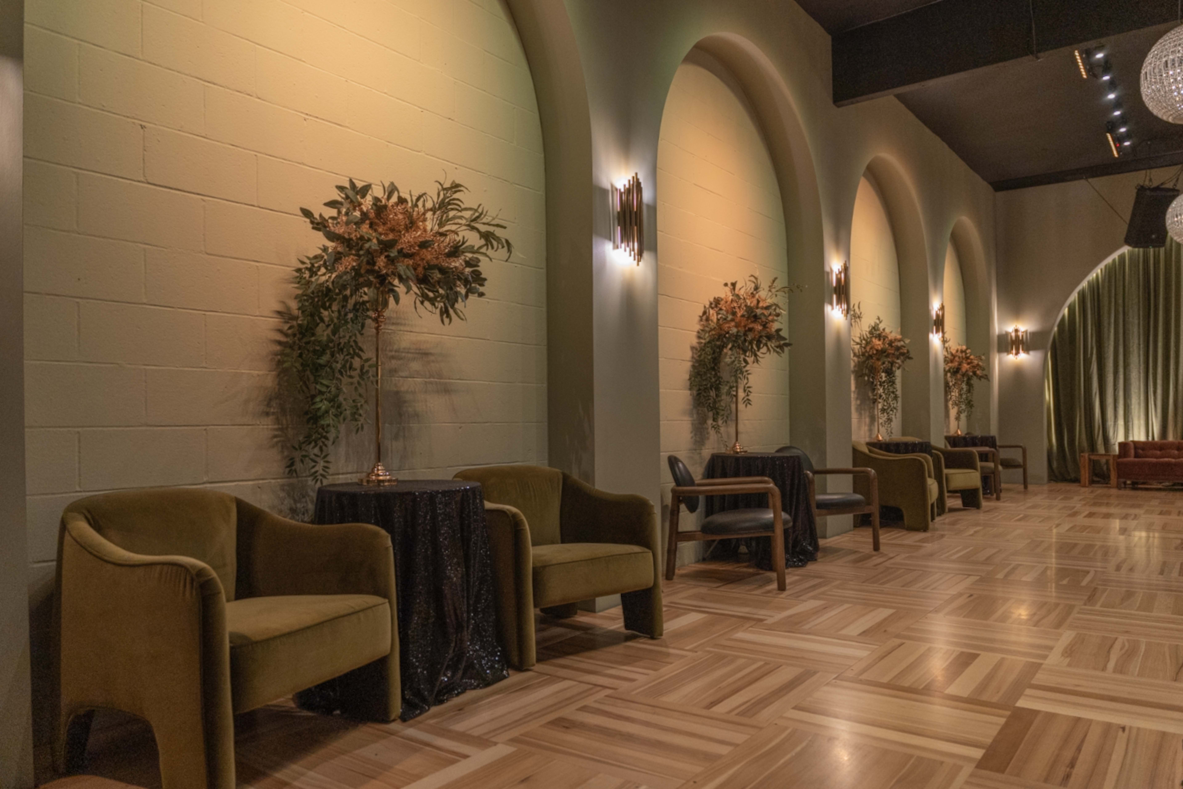 A stylish interior with curved arches and green walls, featuring seating arrangements with small tables and floral decorations.