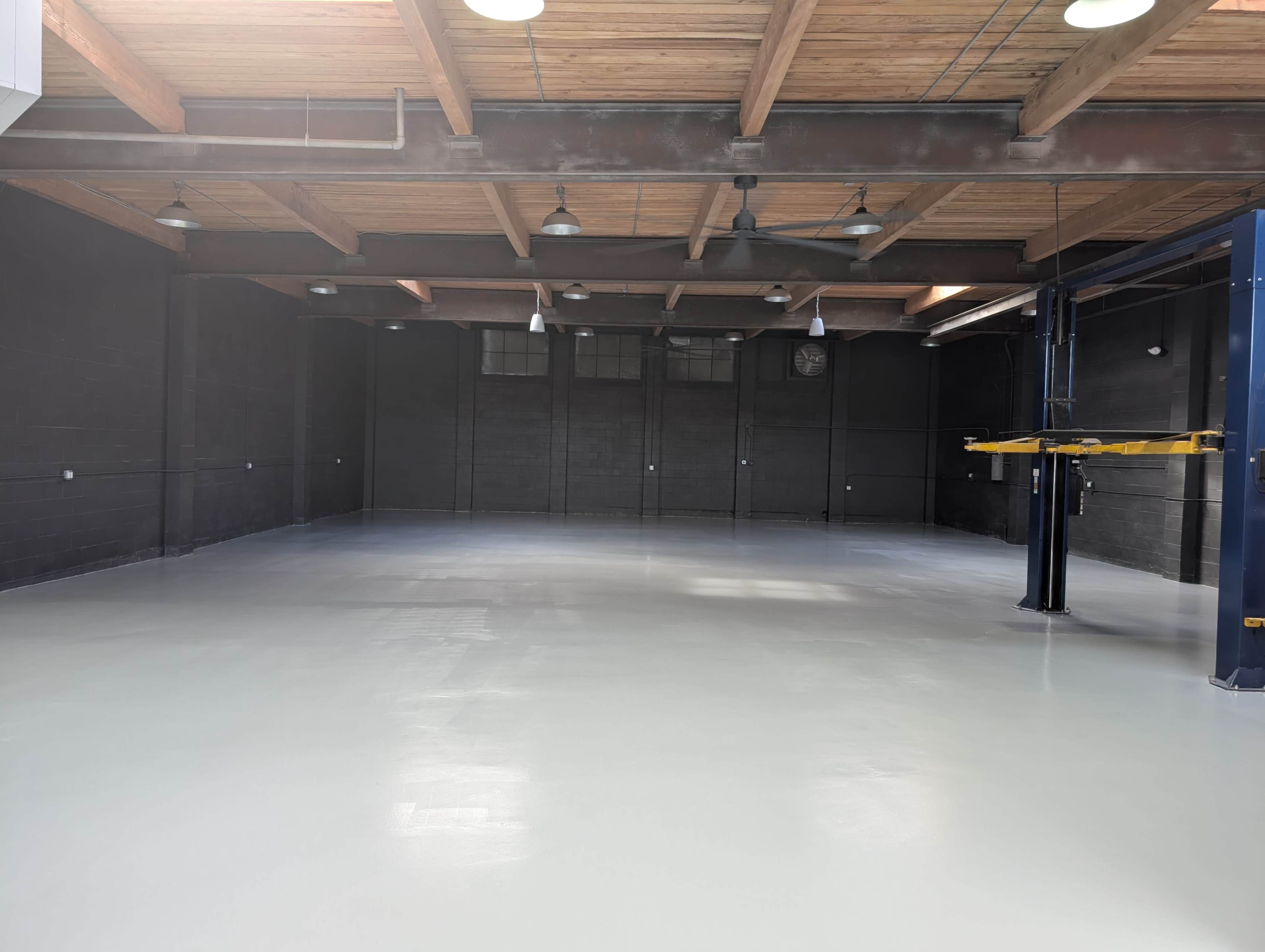 The image shows an empty industrial space with a polished floor, wooden beams on the ceiling, and minimal lighting.