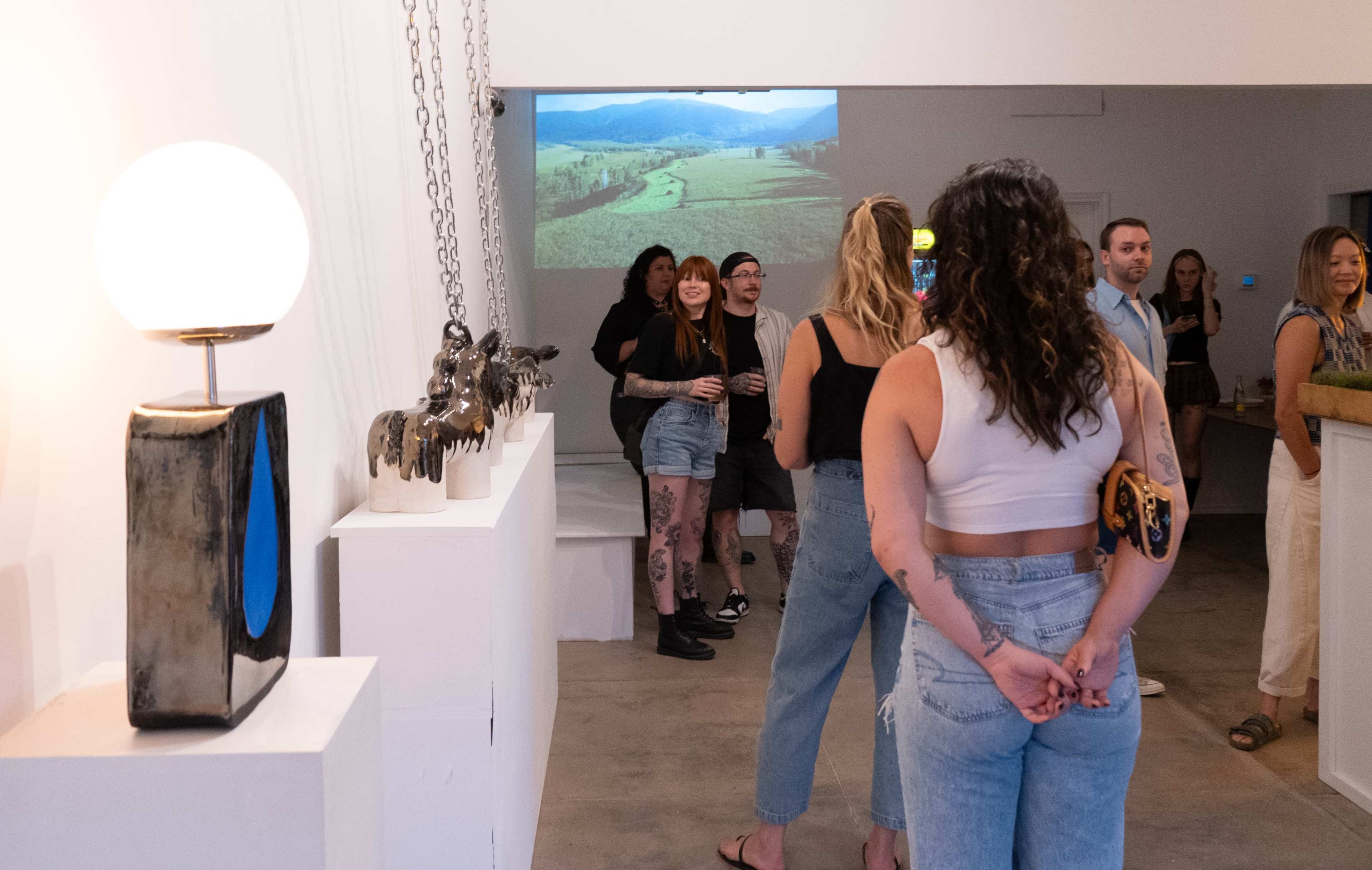 A group of people stands in an art gallery, with a projected landscape image on the wall and various sculptures displayed nearby.