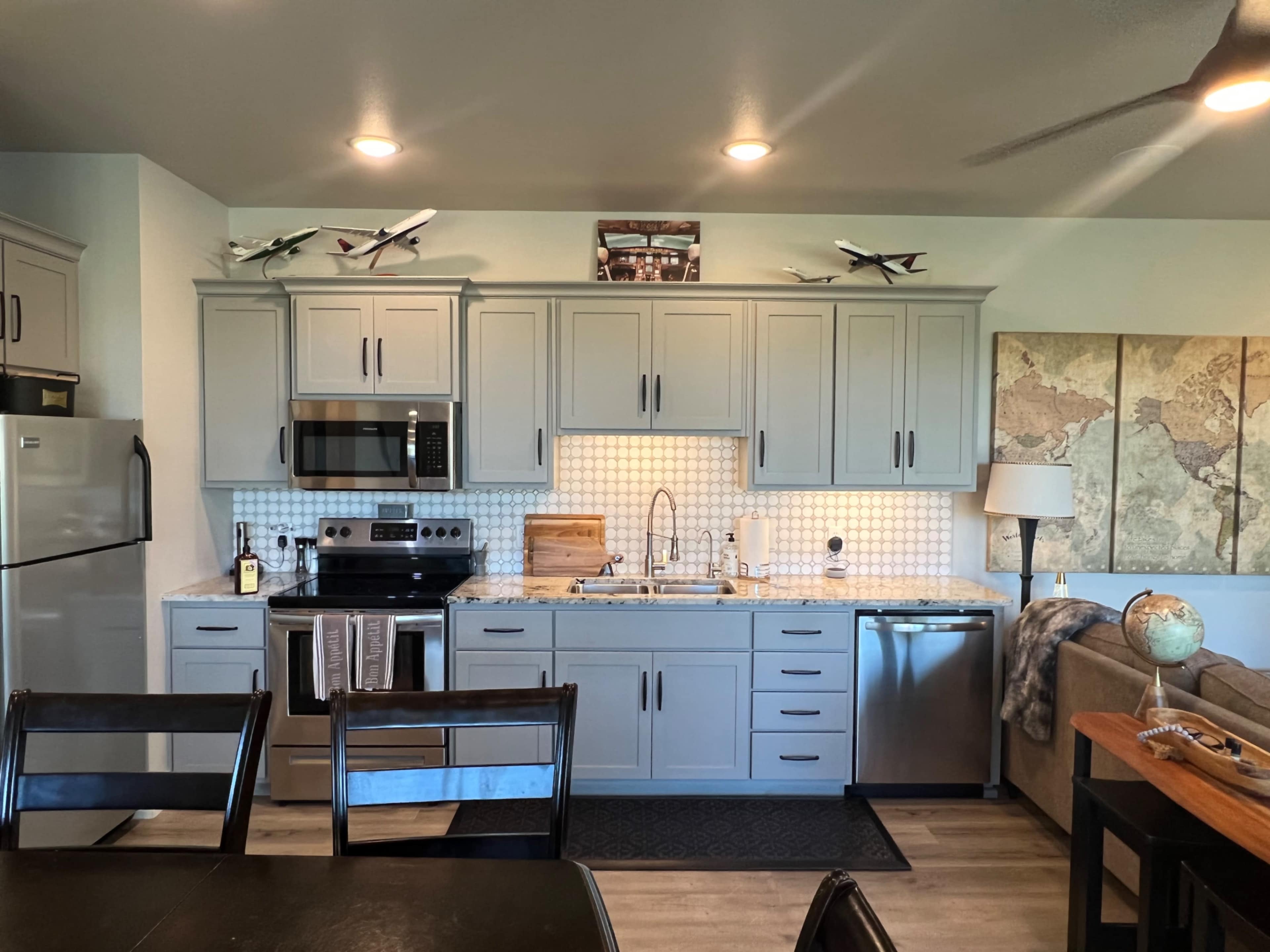 A modern kitchen features gray cabinets, stainless steel appliances, and a decorative map wall above the sink.