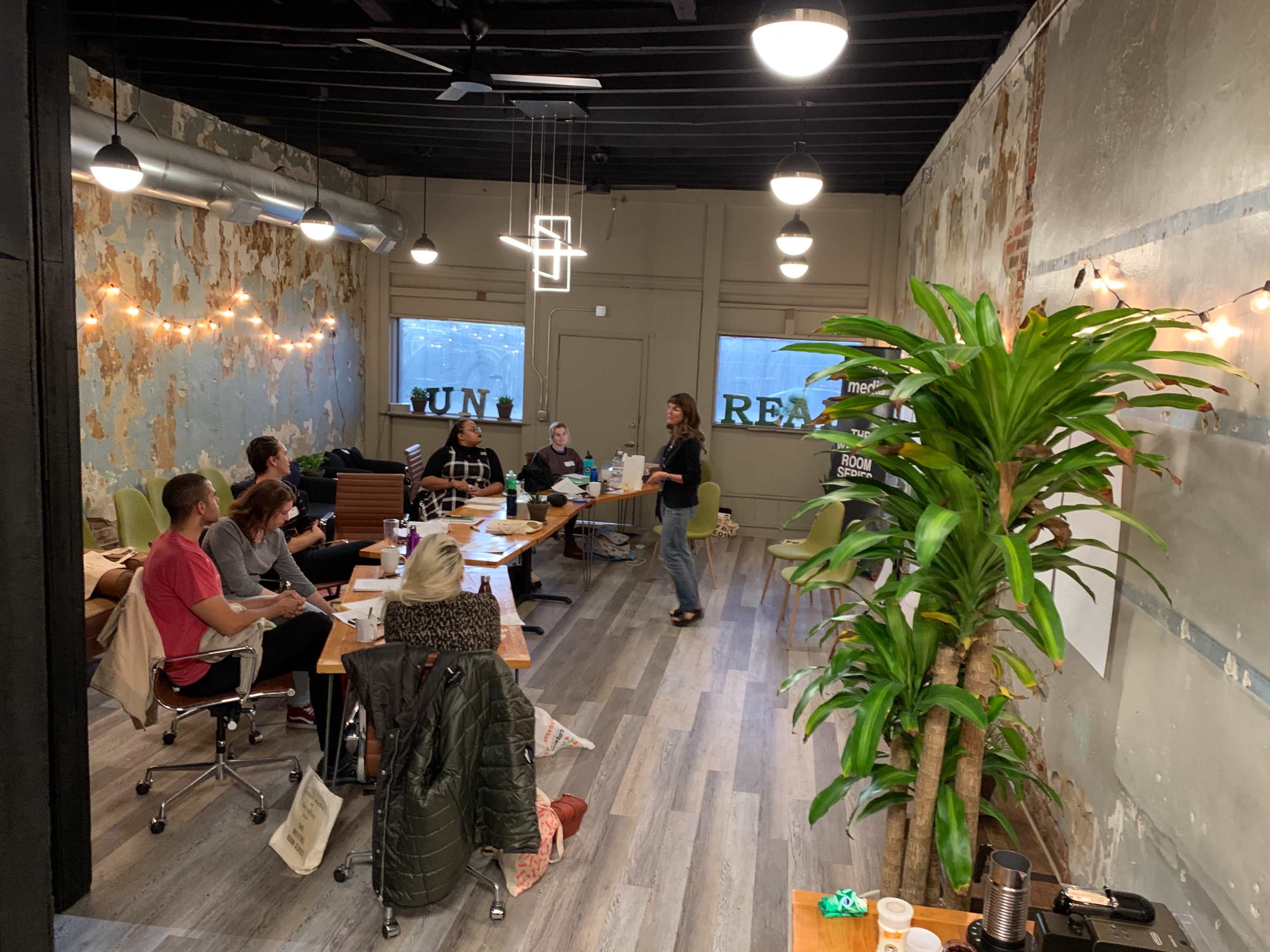 A group of people is engaged in a meeting inside a room with exposed brick walls and modern furnishings.