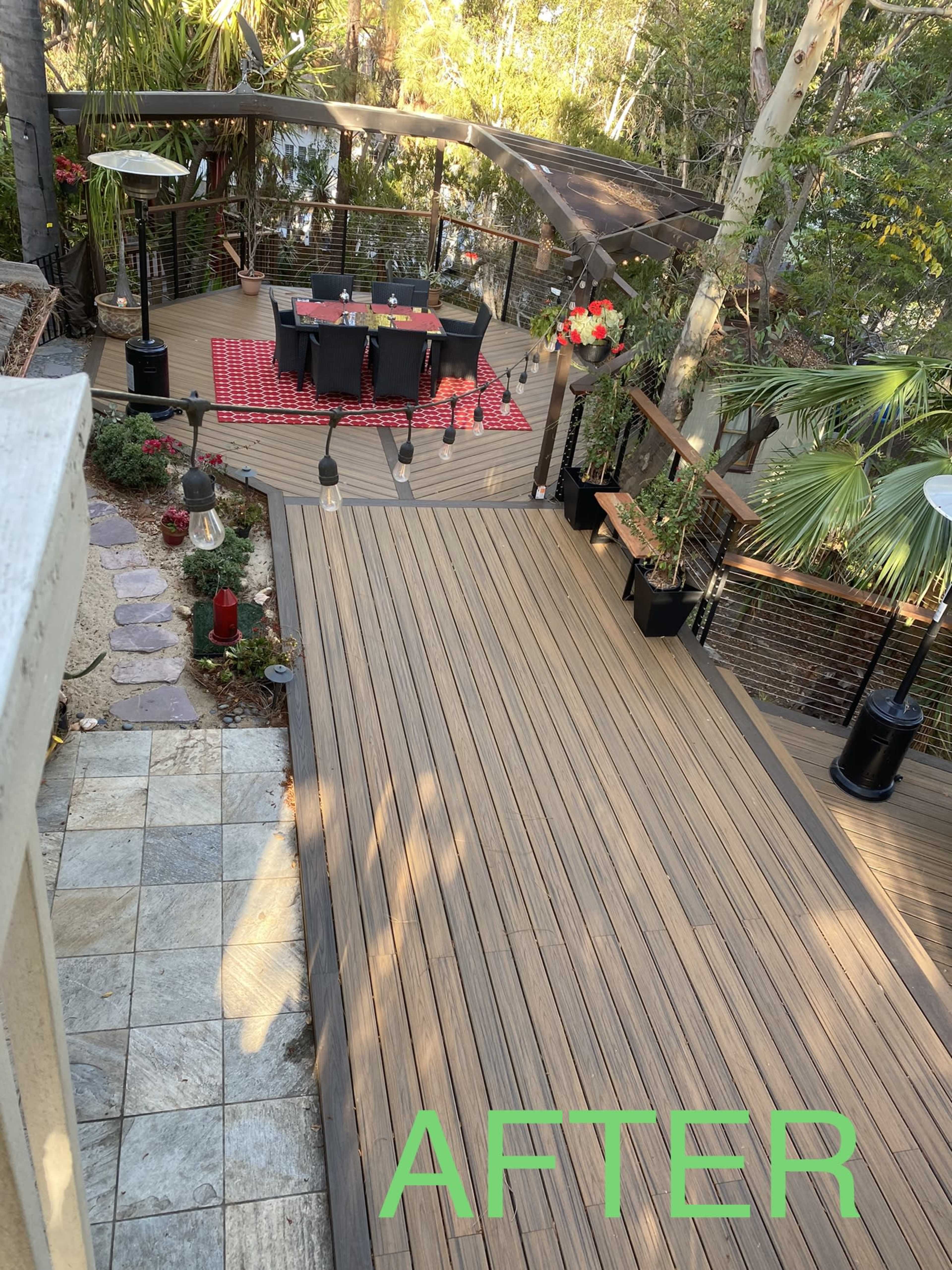 A spacious outdoor deck area with a dining table set for six under a canopy, surrounded by lush greenery and decorative plants.