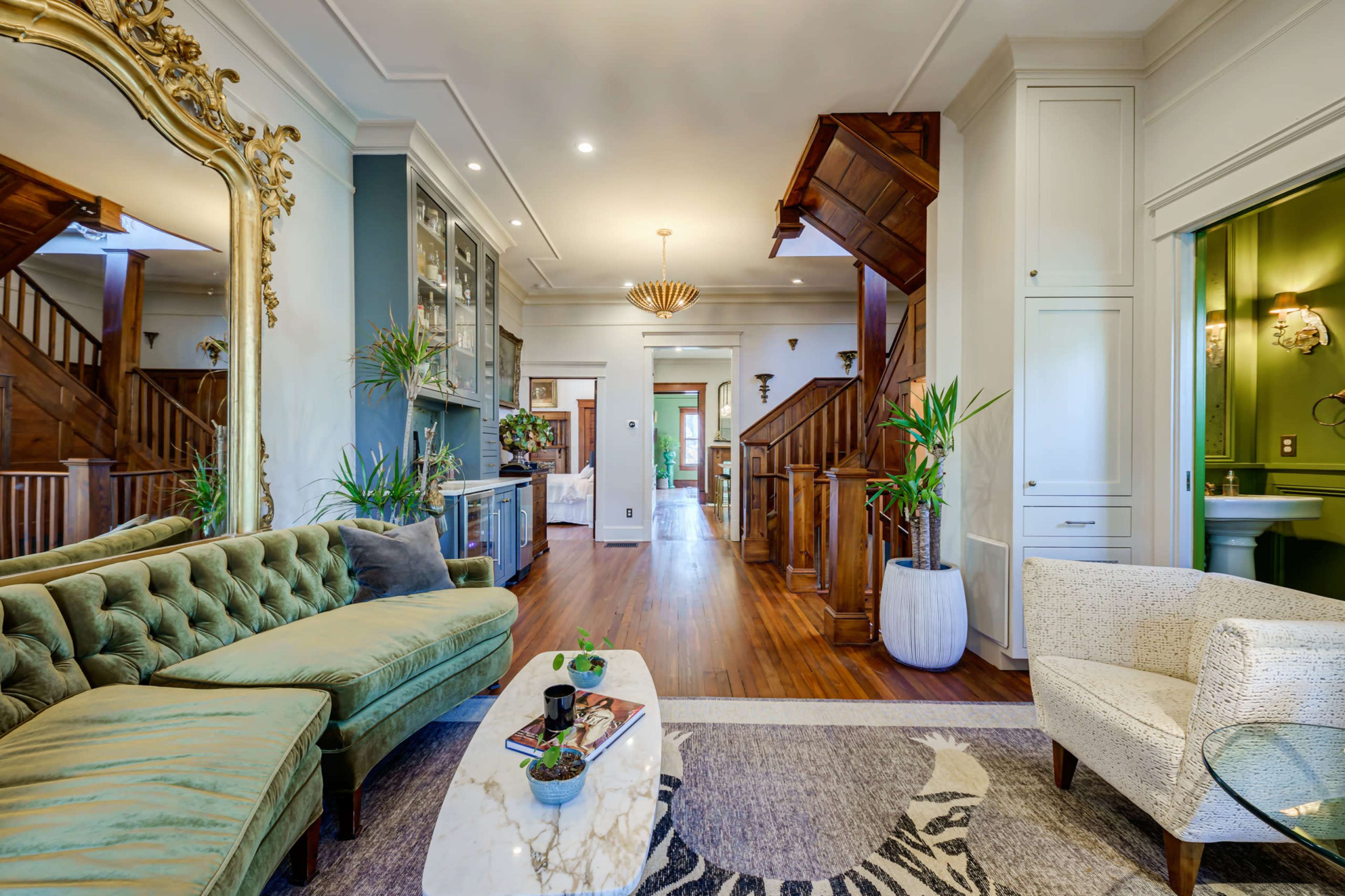 A spacious living room with a green velvet sofa, a marble coffee table, and a view of a staircase leading to other rooms.