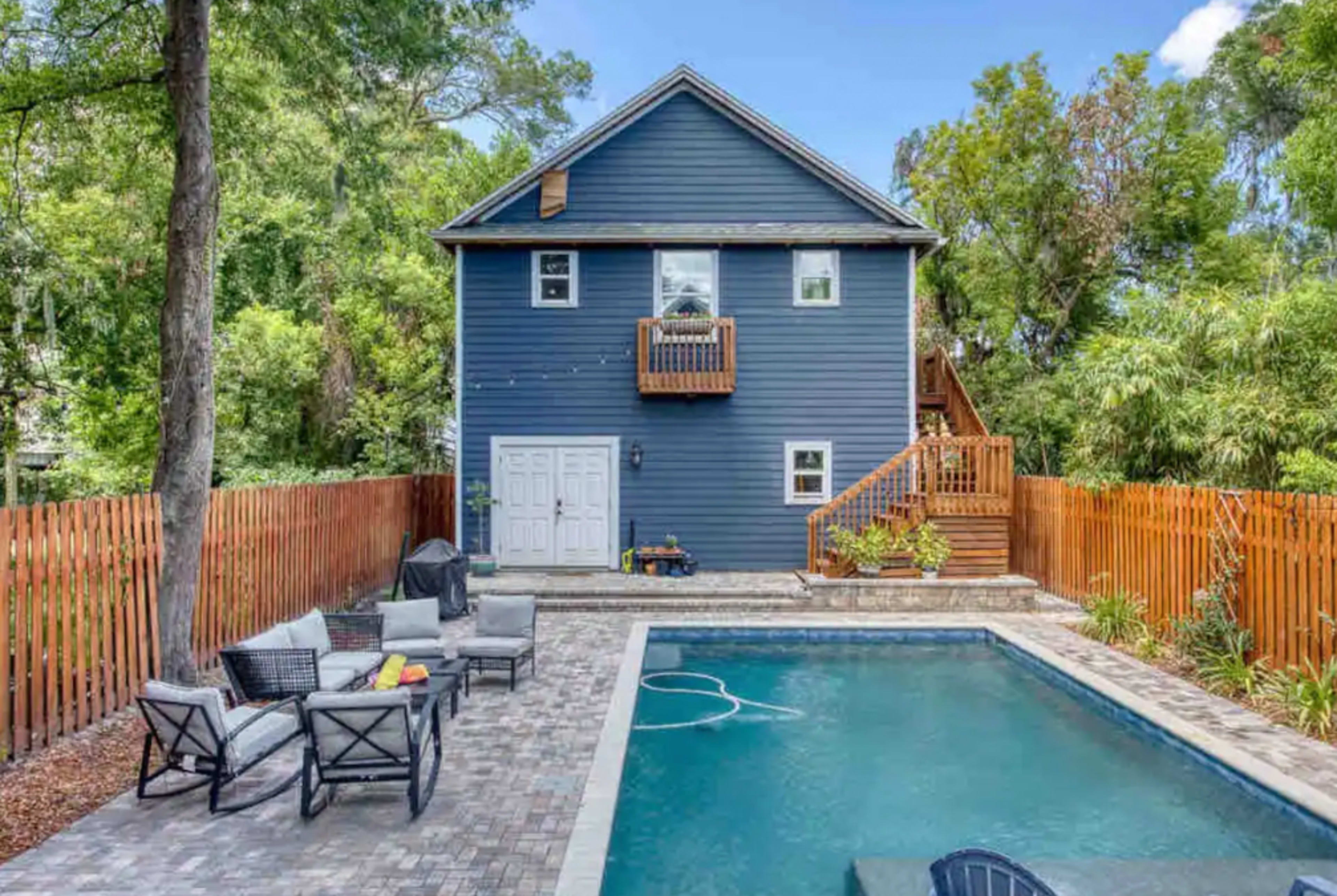 A two-story blue house with a fenced backyard features a swimming pool and a patio area with seating.
