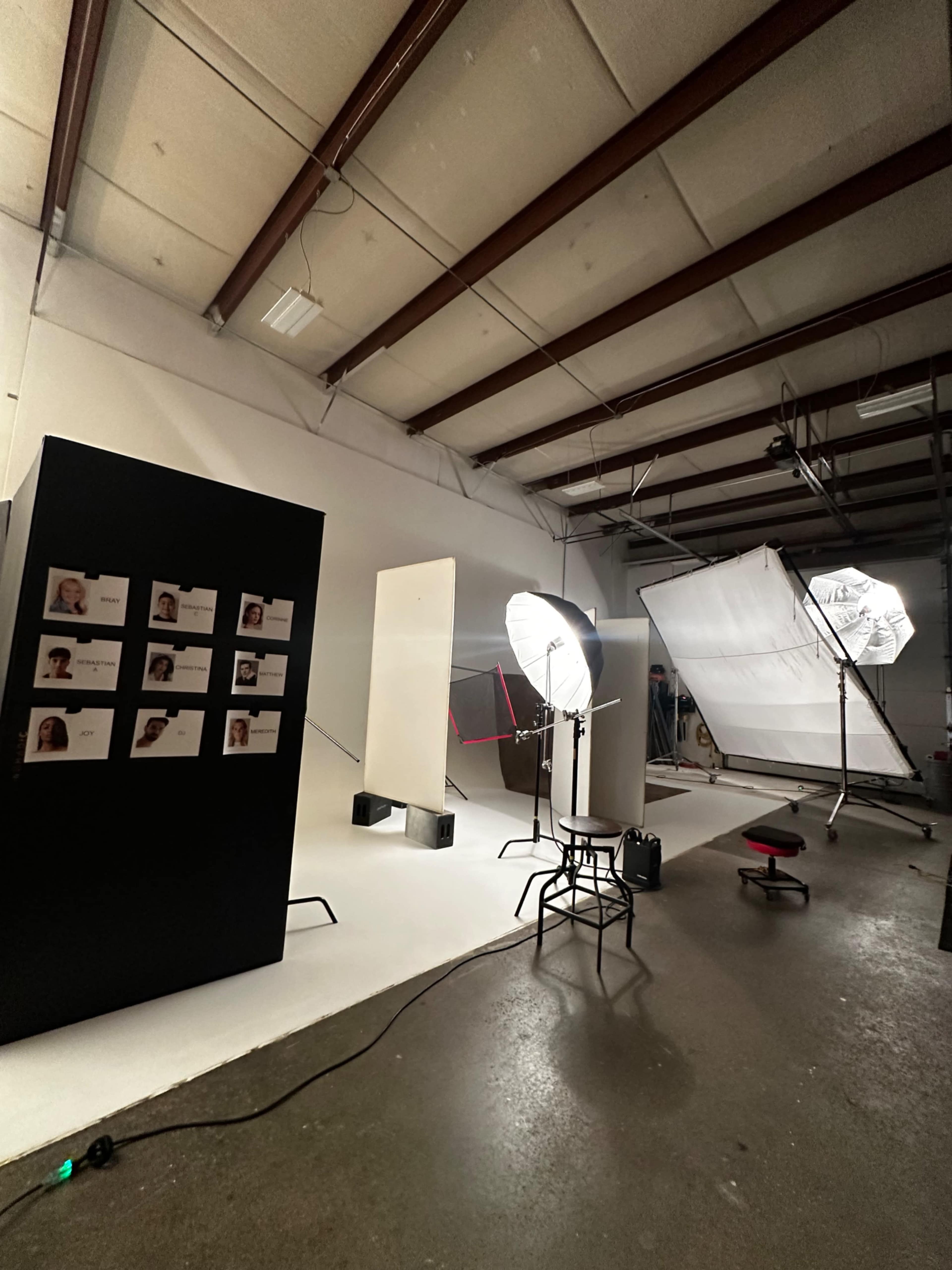 The image shows a photography studio setup with lights, backdrops, and a seating area, accompanied by a display of model portraits on a black panel.