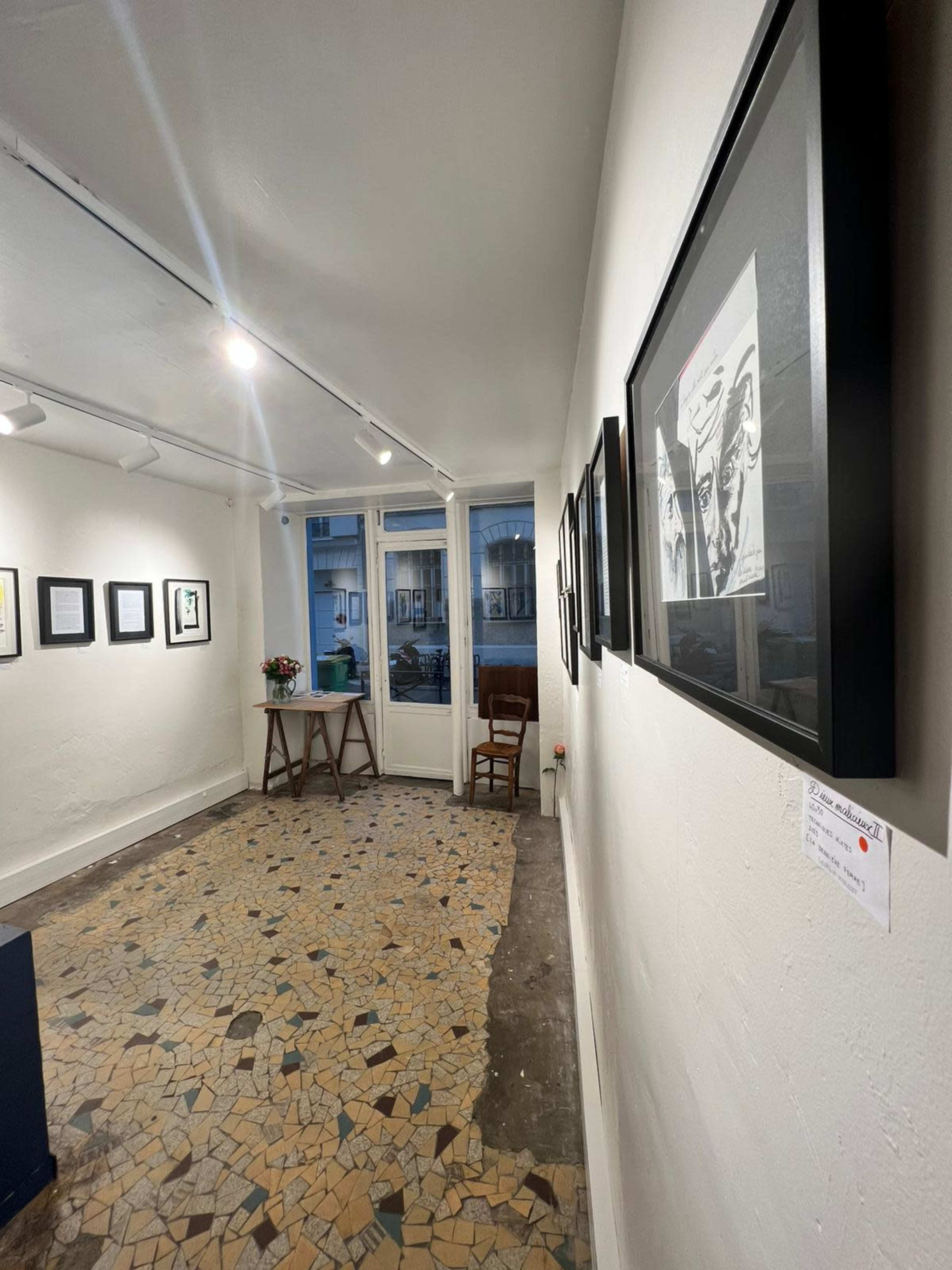 The image shows an art gallery interior with framed artworks on the walls and a patterned tiled floor.