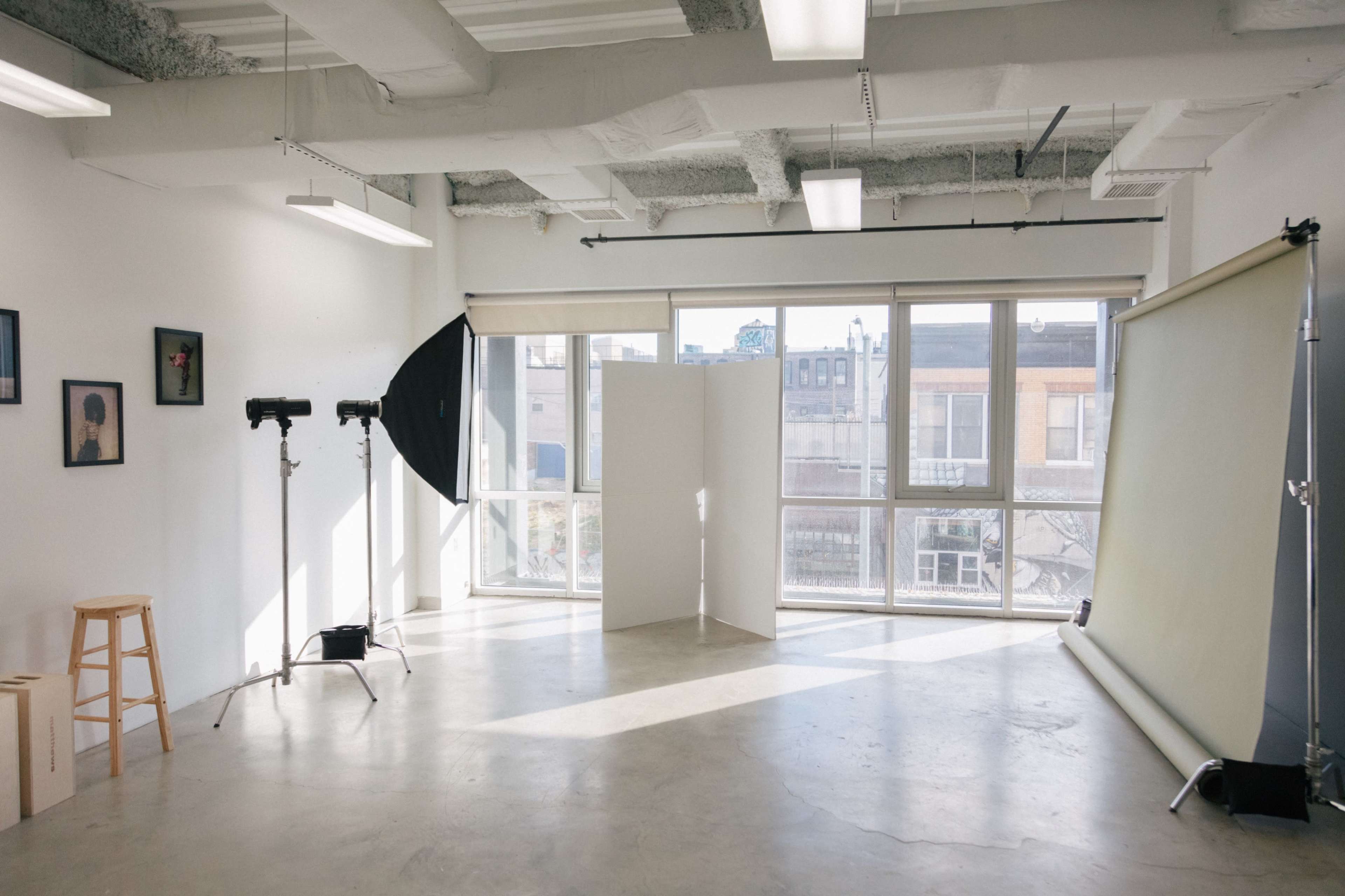 A well-lit photography studio with a backdrop, lighting equipment, and large windows overlooking a cityscape.