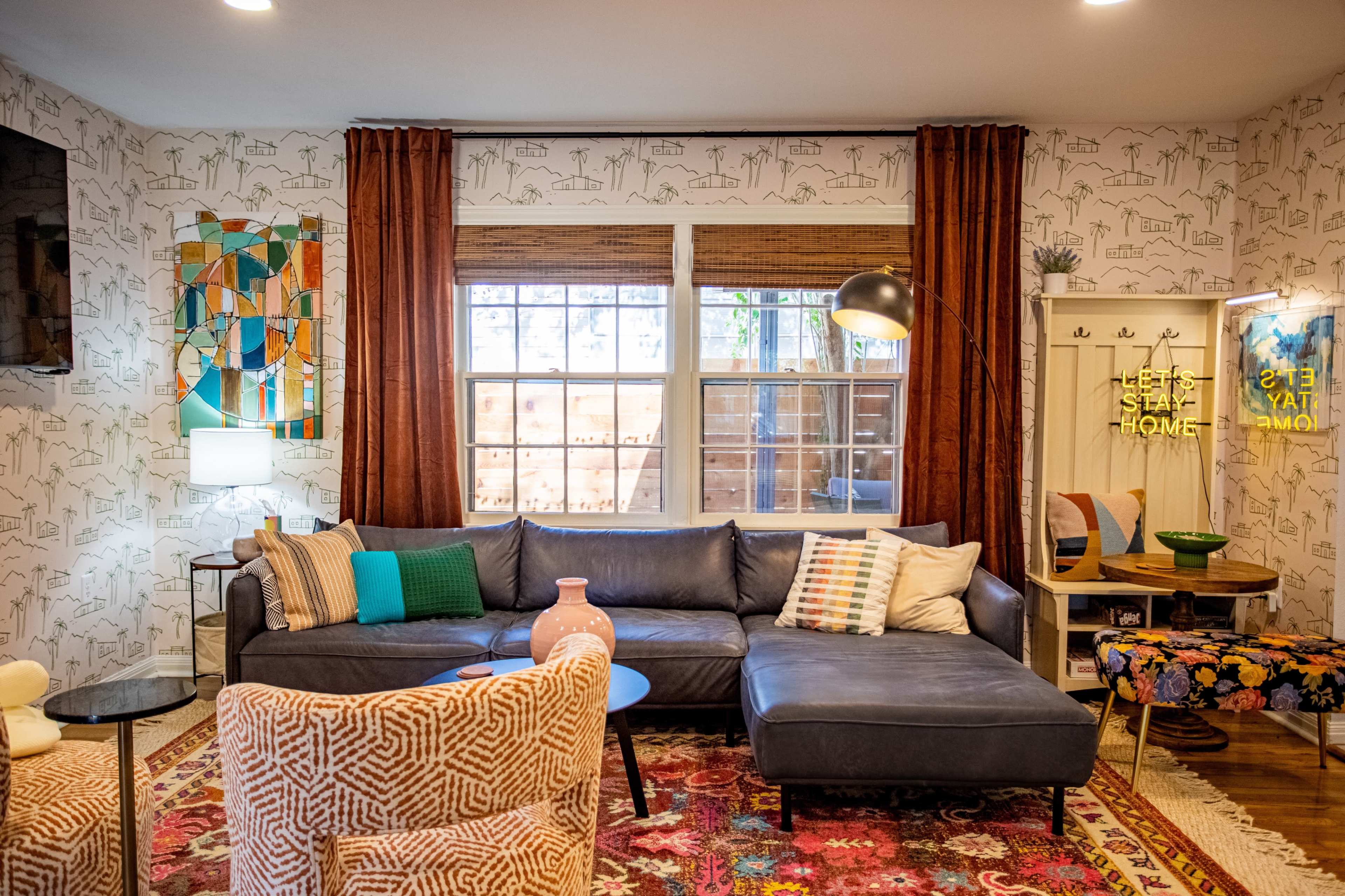 A cozy living room features a dark blue sectional sofa, patterned rugs, and decorative elements like a floor lamp, art on the walls, and a mix of colorful pillows.