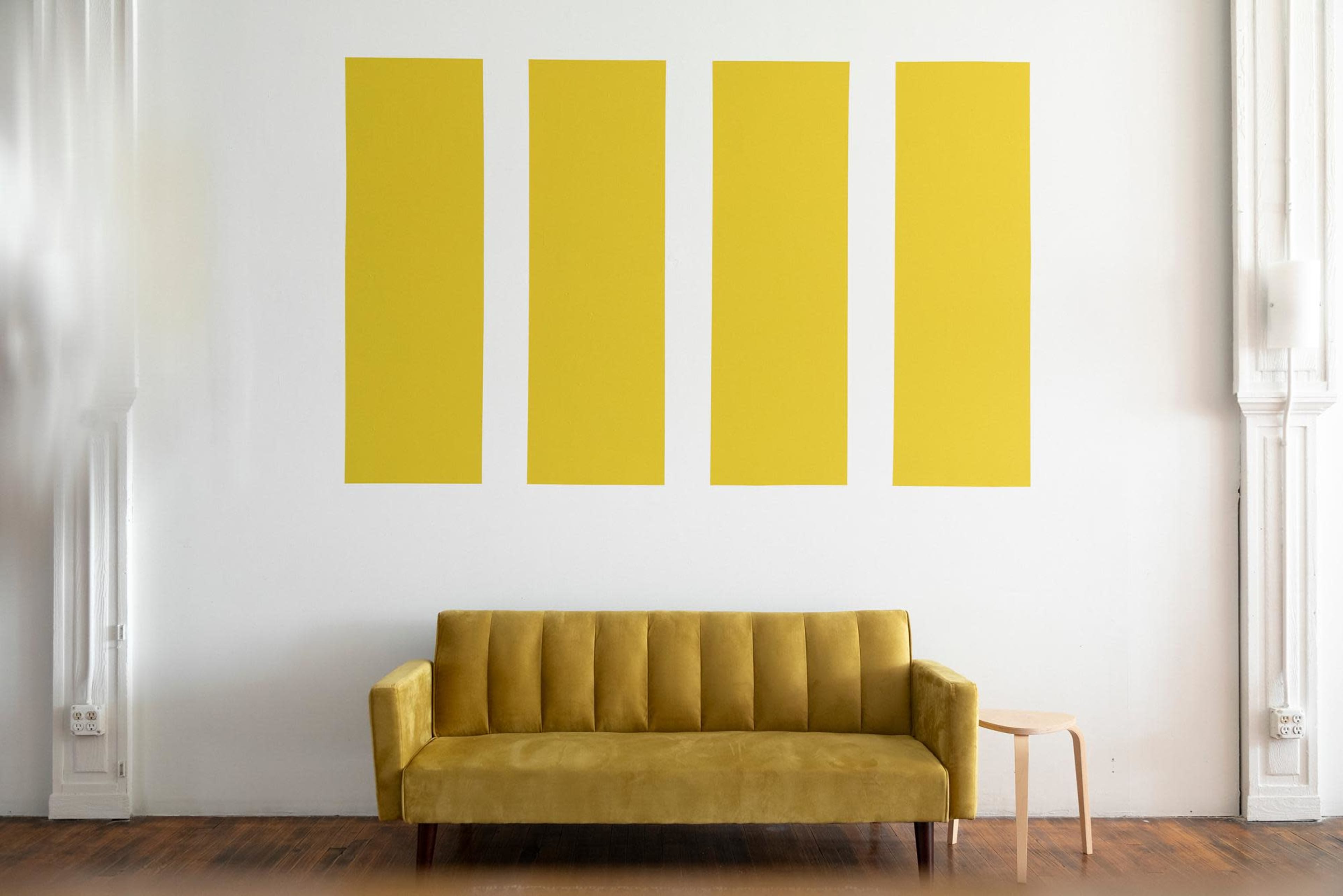 A yellow sofa is positioned in front of a wall featuring four vertical yellow panels.