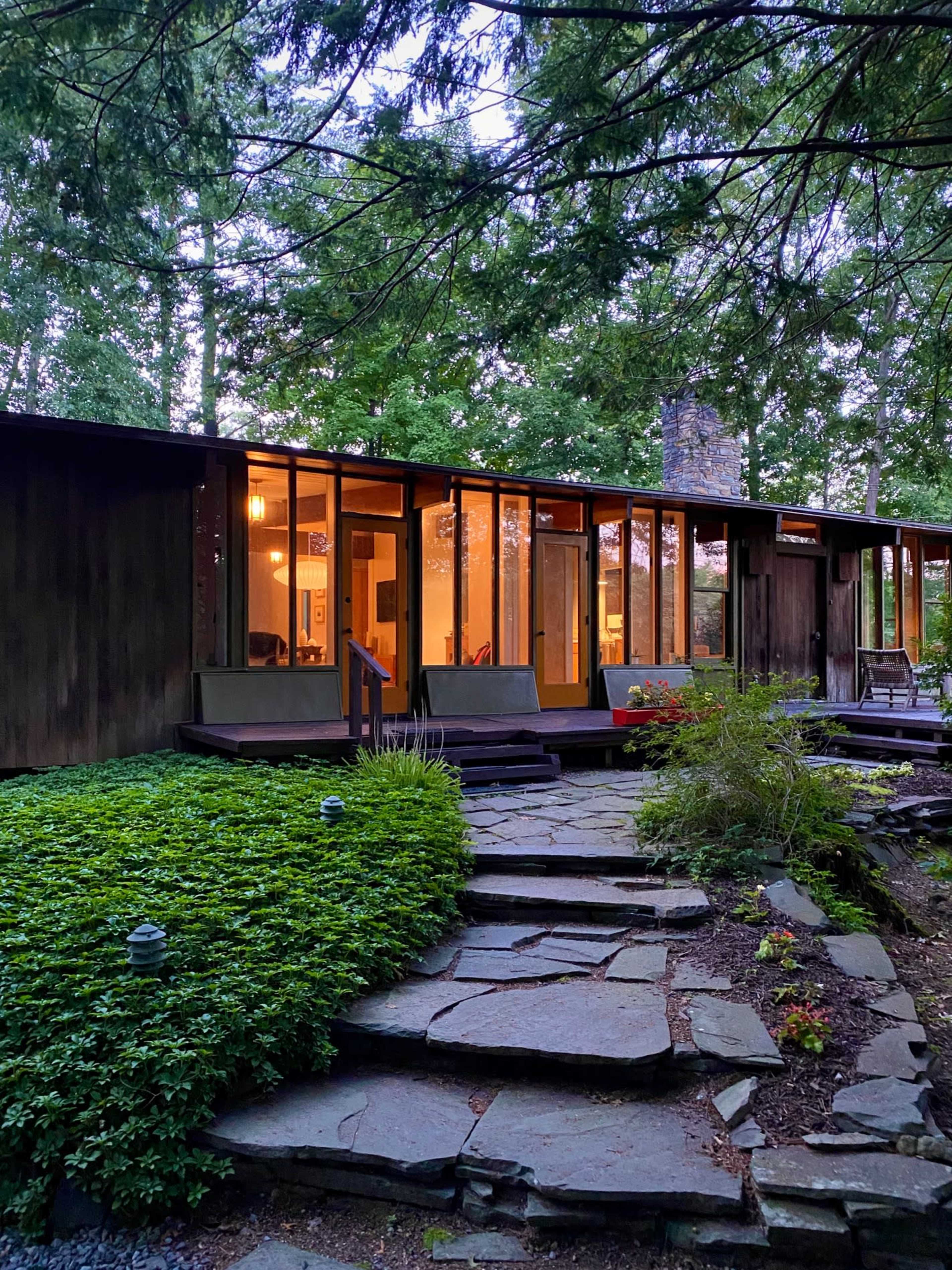 A modern house with large windows and a stone pathway surrounded by greenery.
