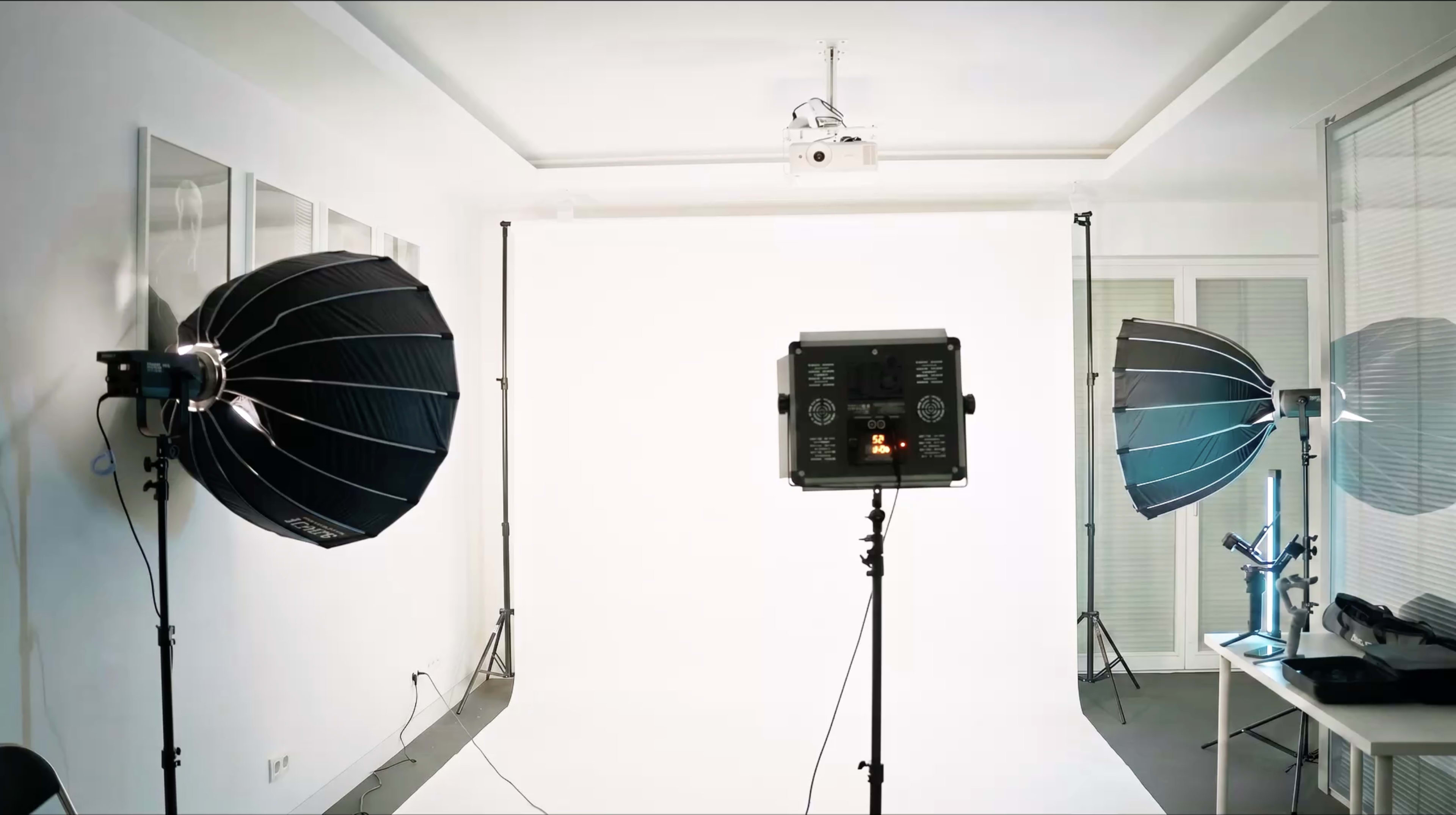 The image shows a photography studio with two large softbox lights on either side and a blank white backdrop in the center.