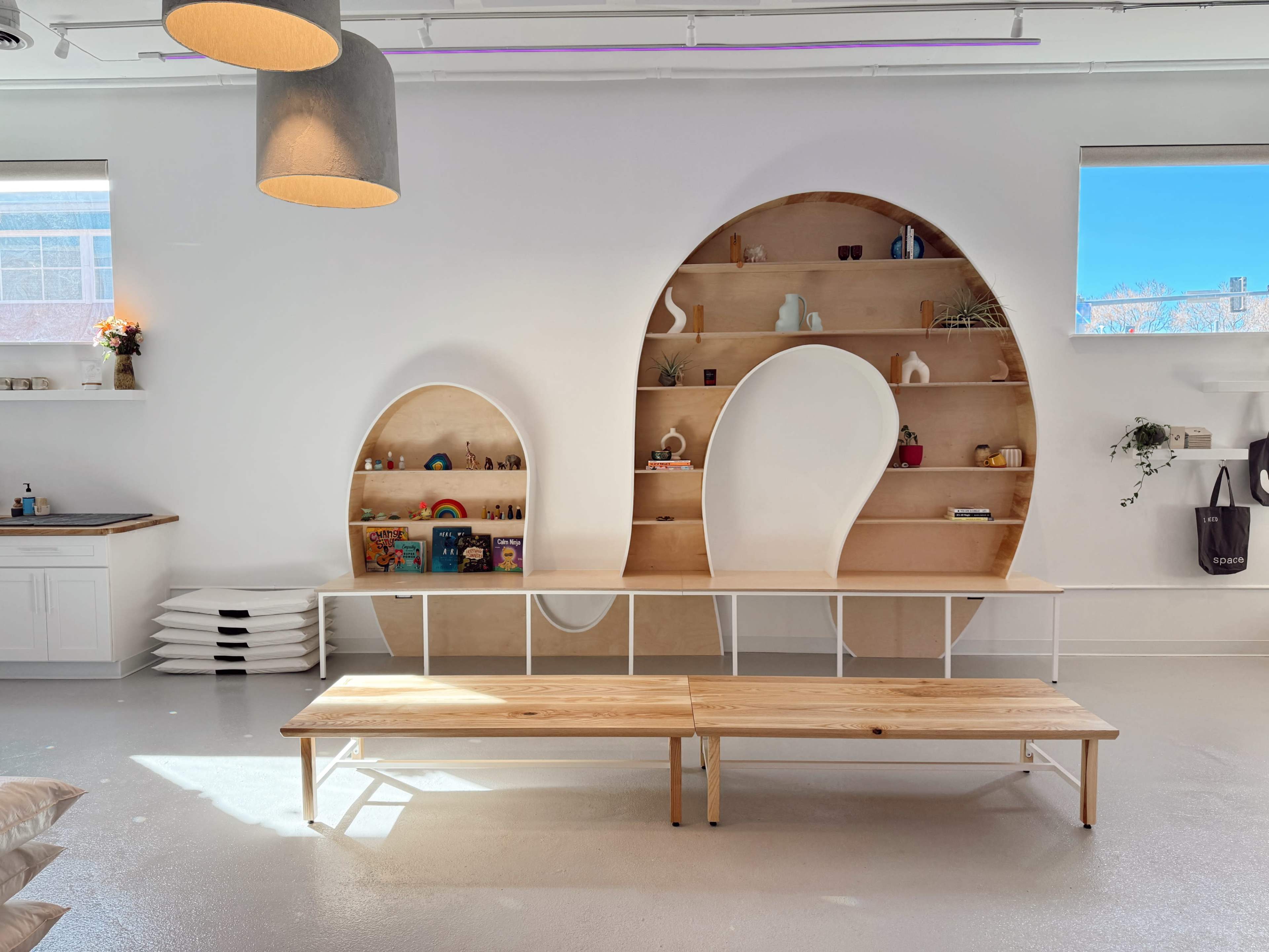 The image shows a modern interior space featuring a wooden shelf with curved cutouts, a light wooden bench in front, and minimalistic decor.