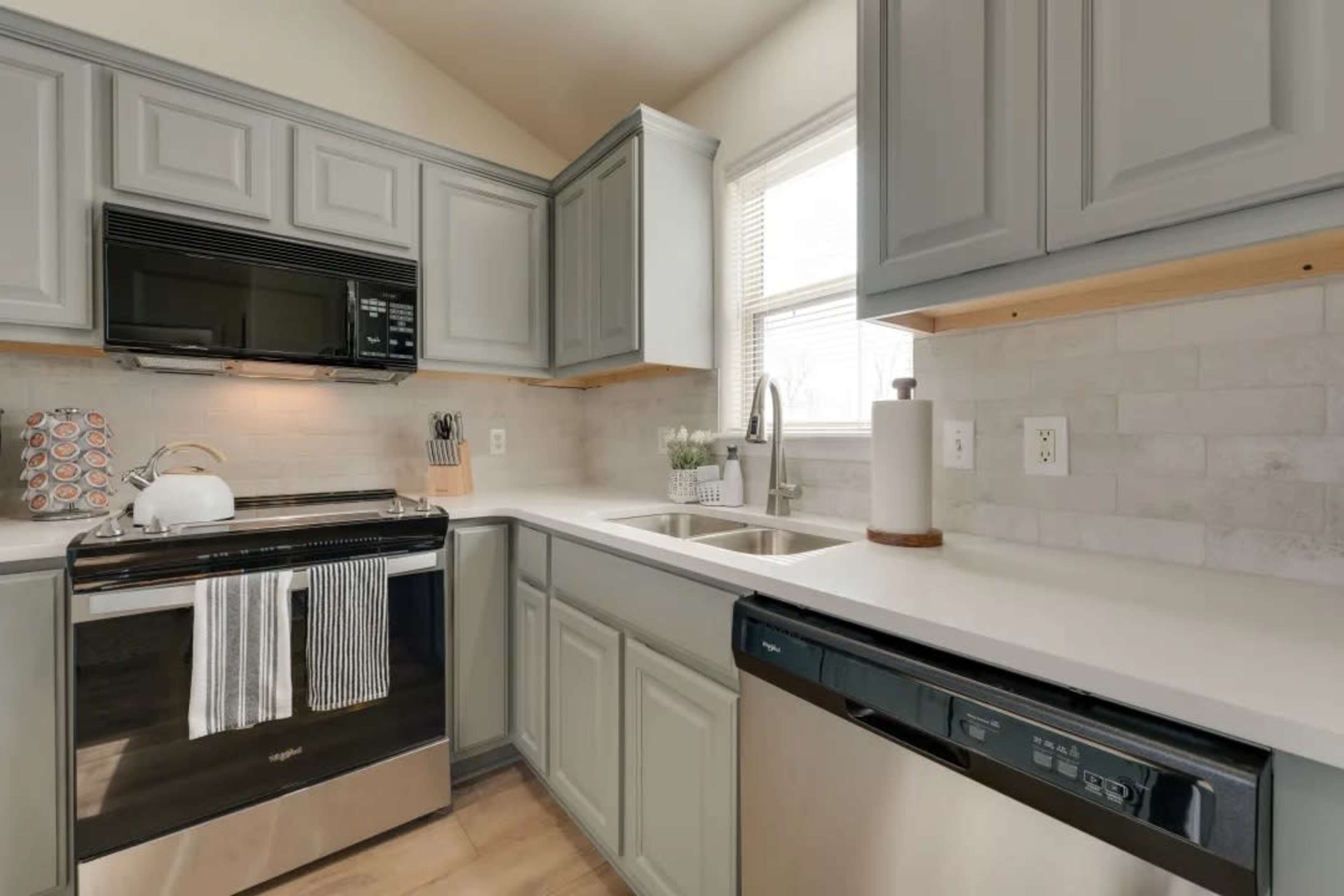 A kitchen with light gray cabinets, a black stove, a silver dishwasher, and a double sink under a window.