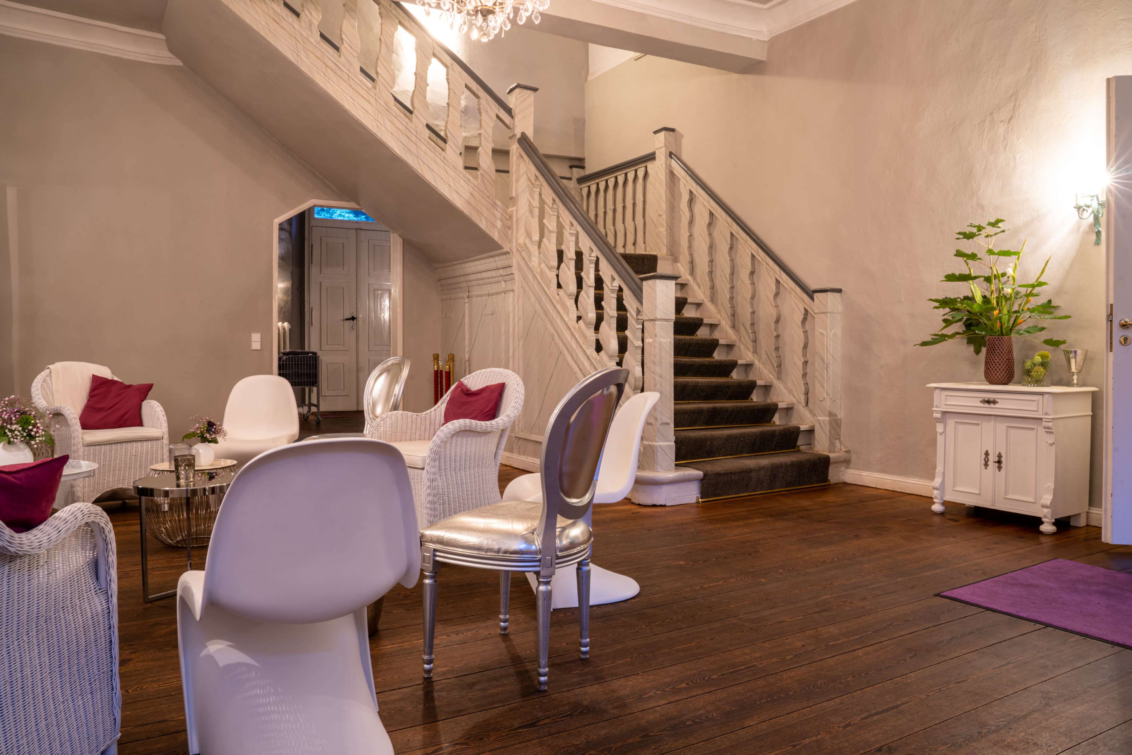 A stylish interior featuring a staircase, seating area with white chairs, and a decorative plant in a corner.