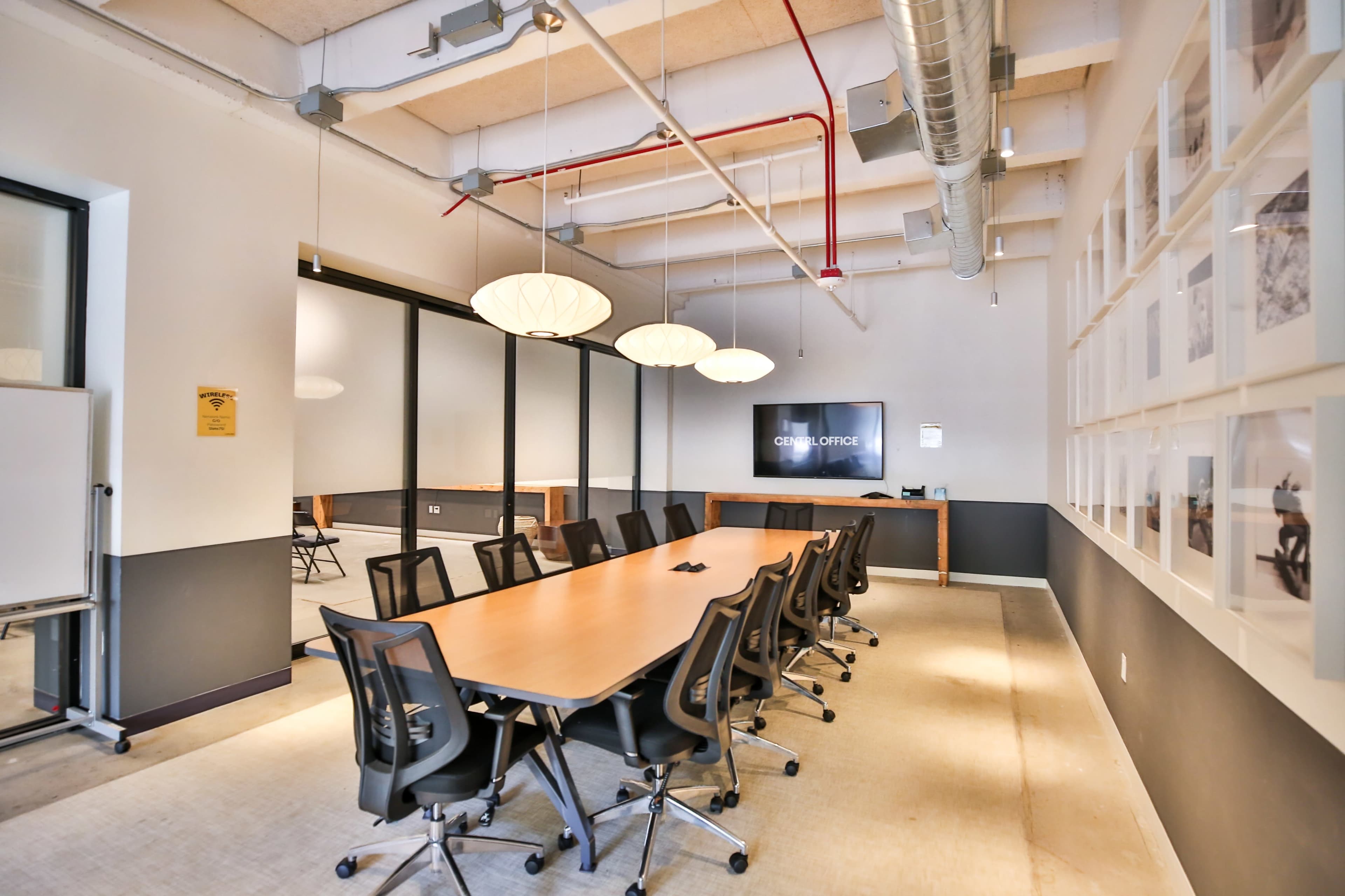 A modern conference room with a long table, multiple chairs, and framed photographs on the wall.