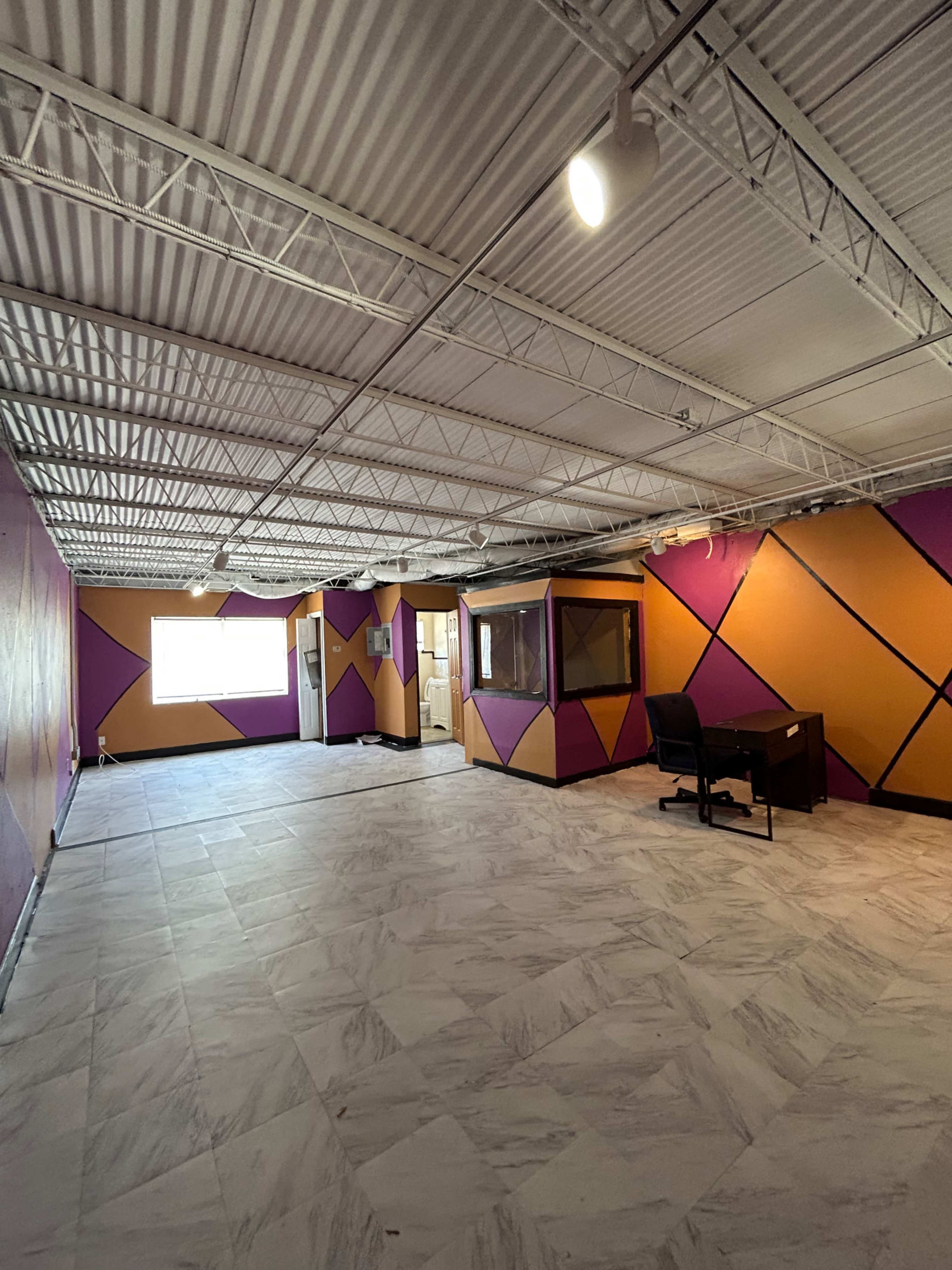 An empty room with purple and gold geometric wall patterns and a dark desk with a chair.