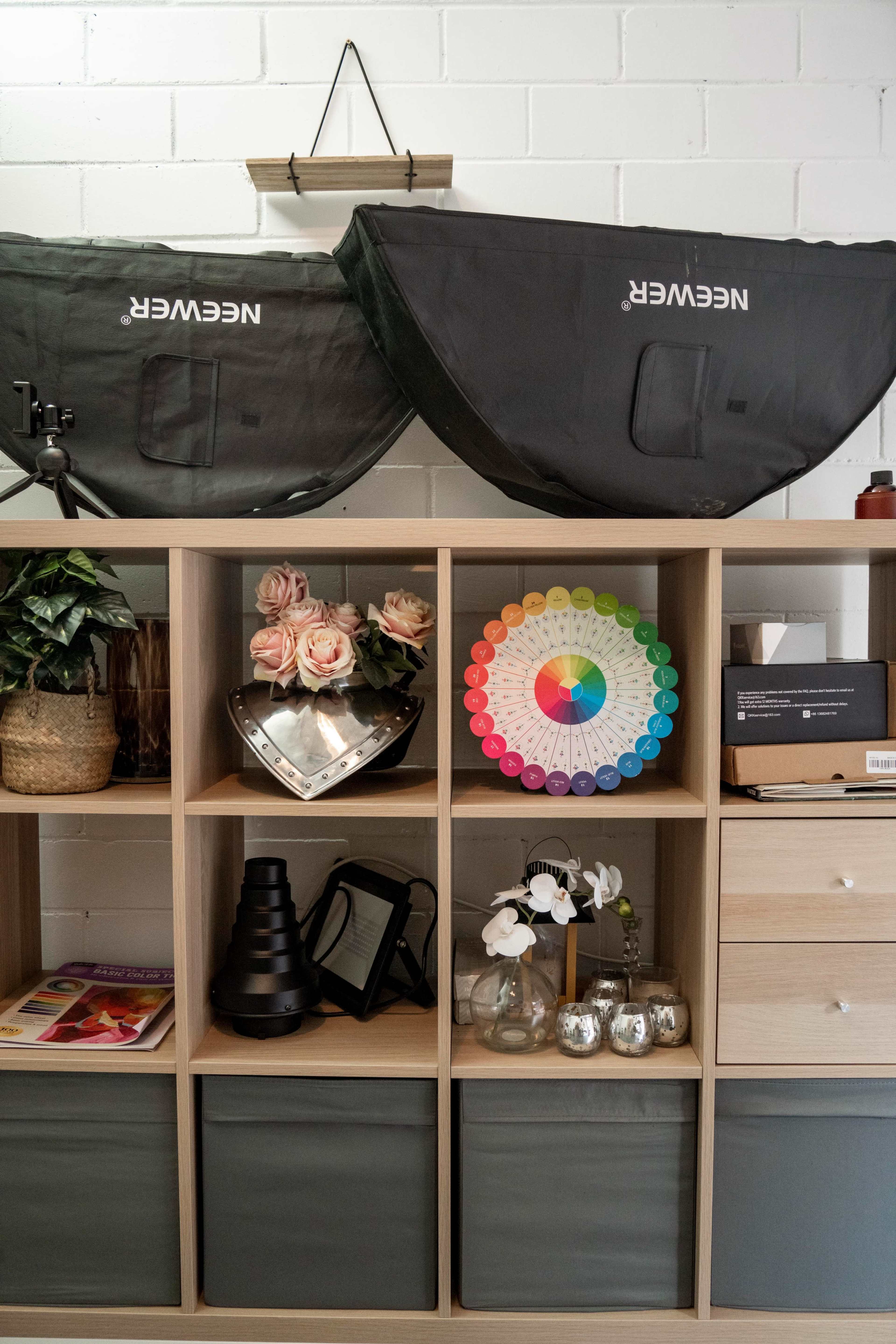 A shelving unit with storage boxes, decorative flowers, a color wheel, and various photography equipment on display.