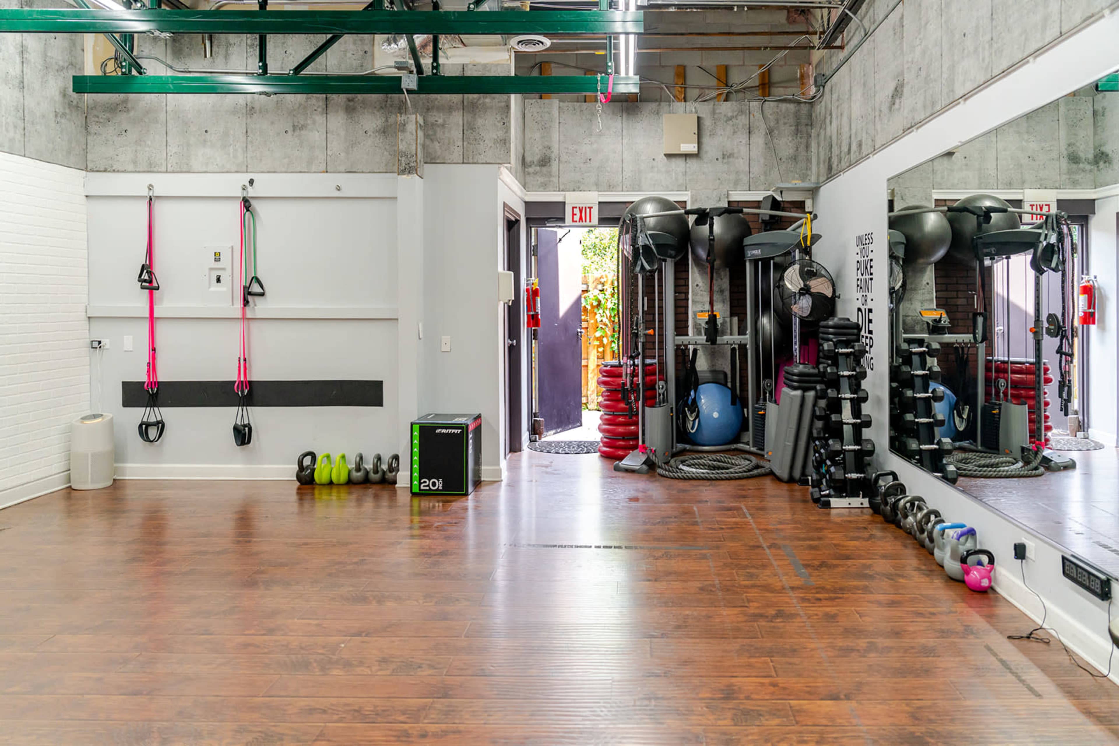 The image shows a spacious gym area with workout equipment, including resistance bands, weights, and a mirror, along with an entrance that opens to an outdoor space.