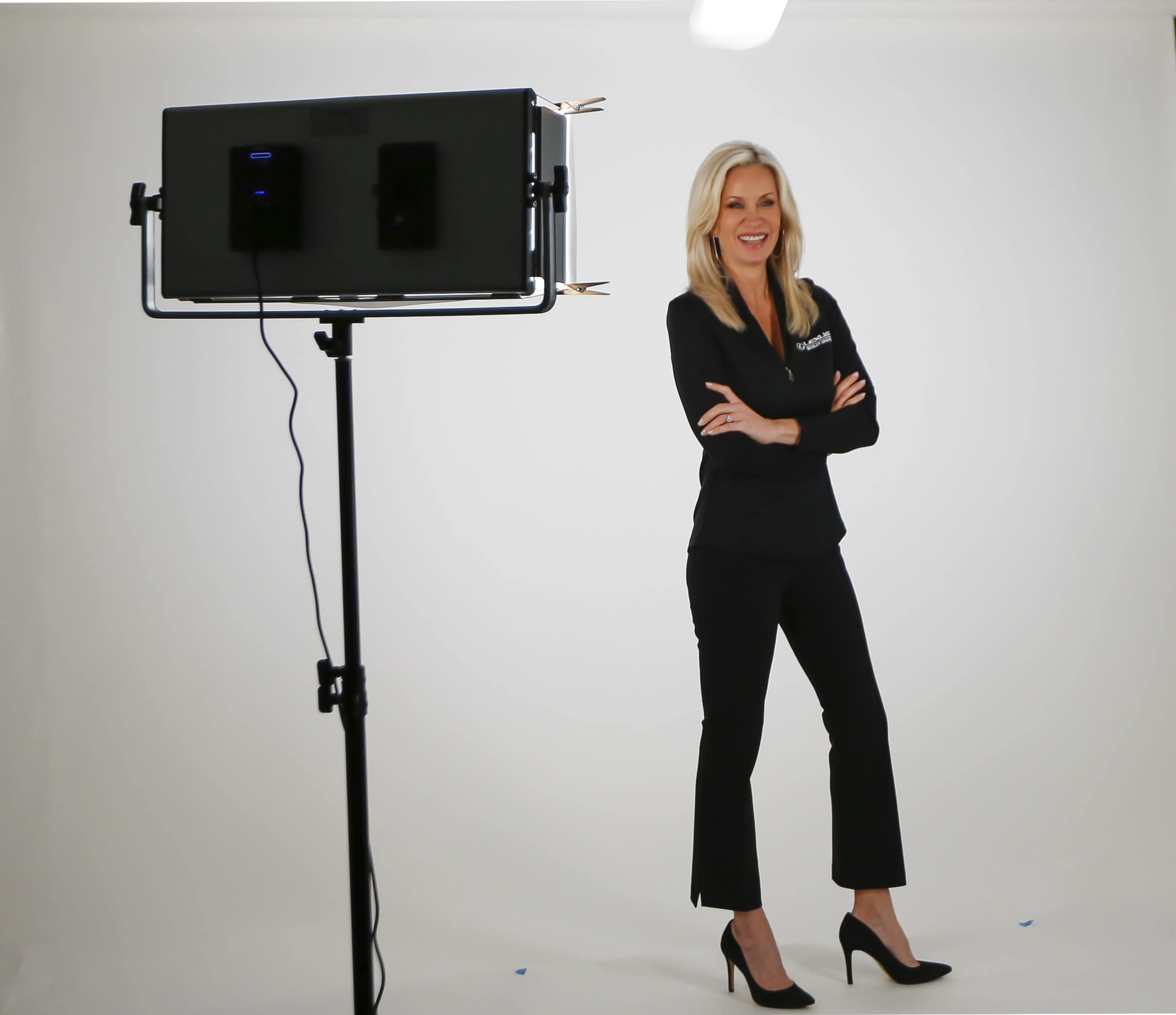 A woman stands confidently with her arms crossed in front of a studio light on a simple white backdrop.