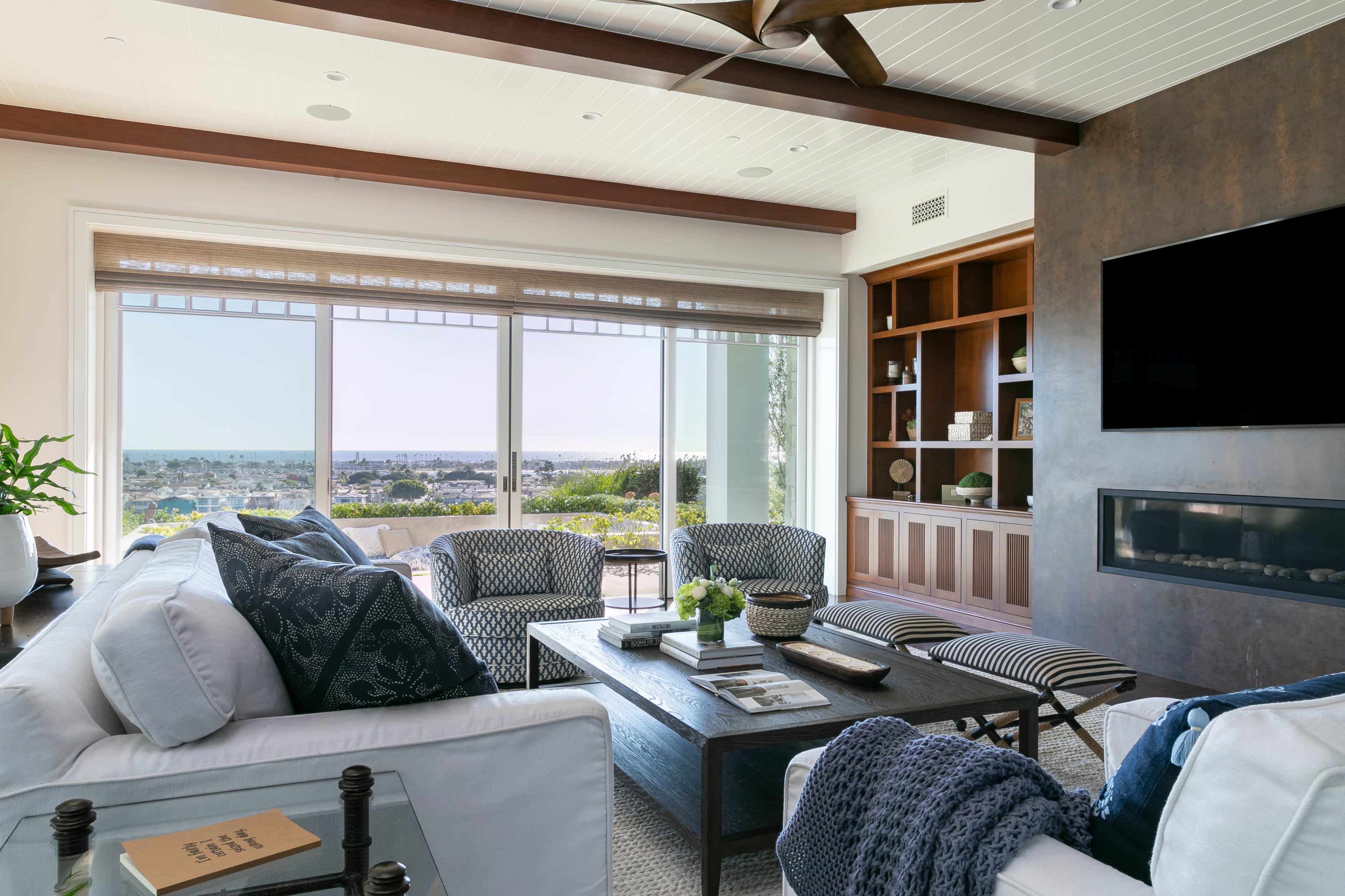 A modern living room features a sectional sofa, accent chairs, and a coffee table, all arranged around a large window with a view of the outdoors.
