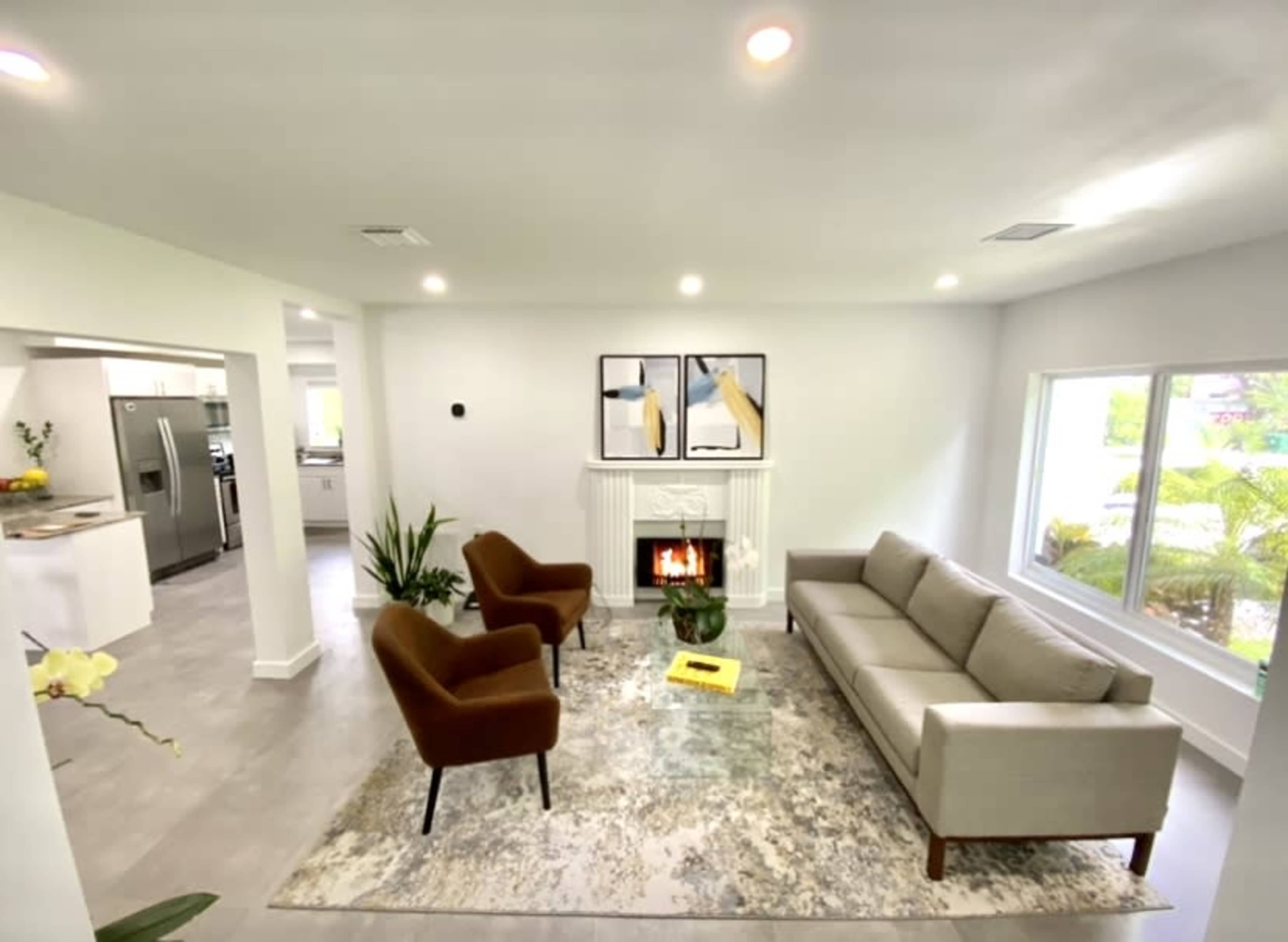 A modern living room with a sofa and two armchairs arranged around a rug near a fireplace, with large windows providing natural light.