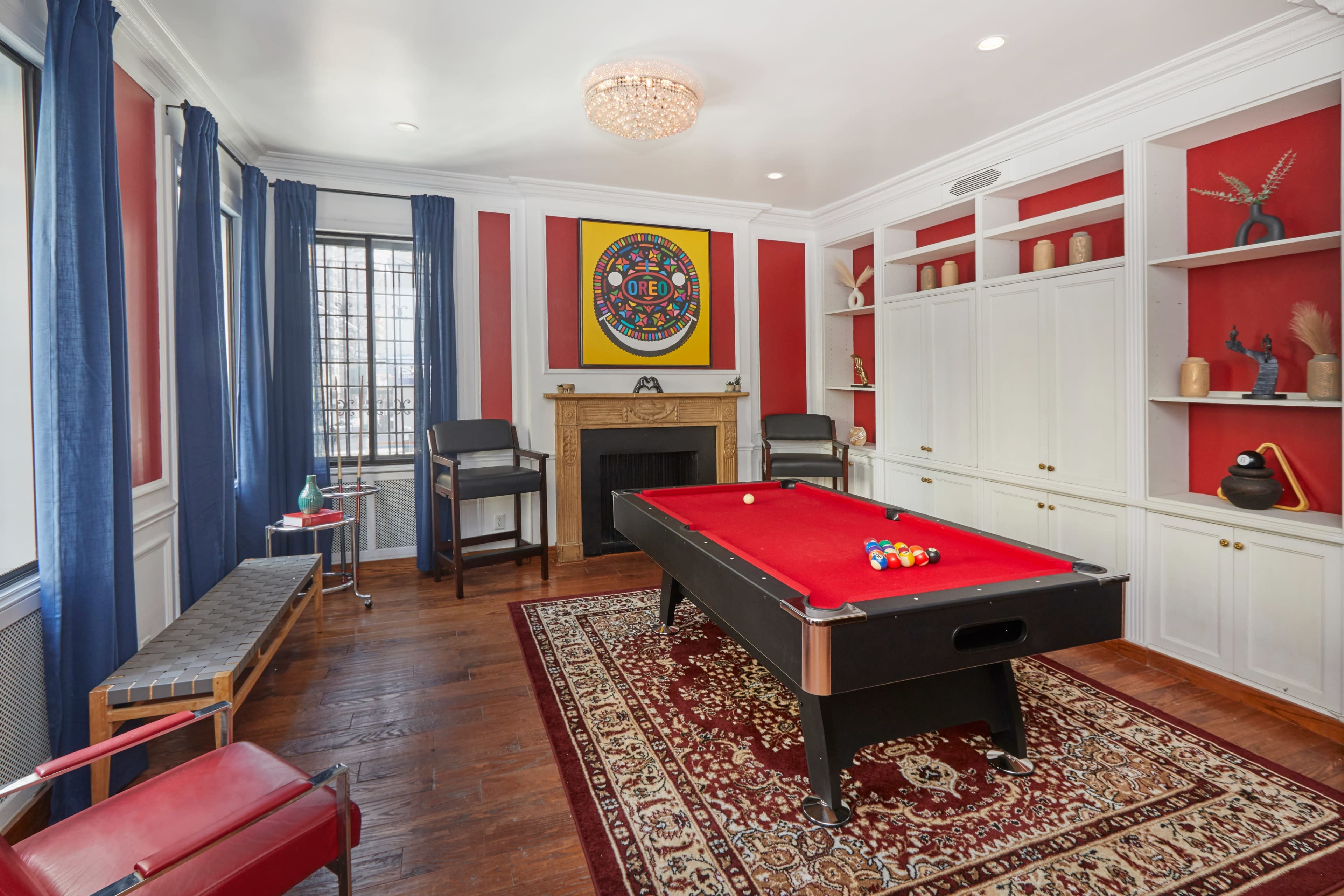 A game room featuring a red felt pool table, a decorative rug, a fireplace, and built-in shelving with various decorative items.