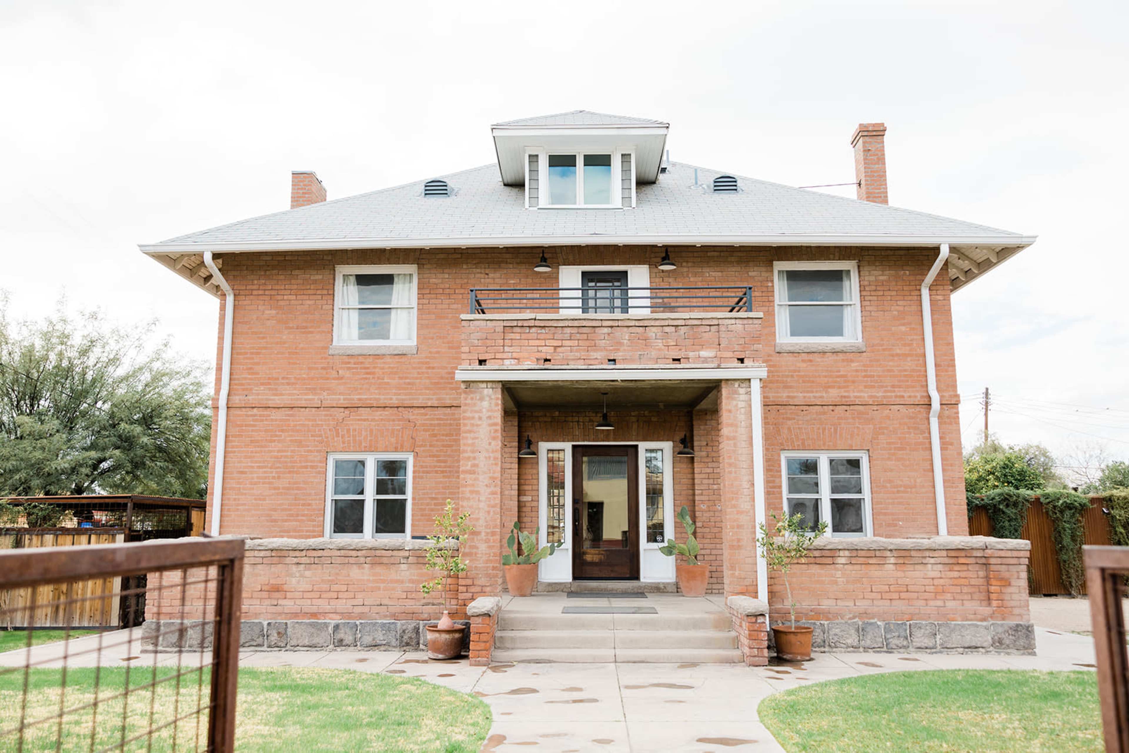 A two-story brick house with a sloped roof, a central entrance, and a small balcony above the front door.
