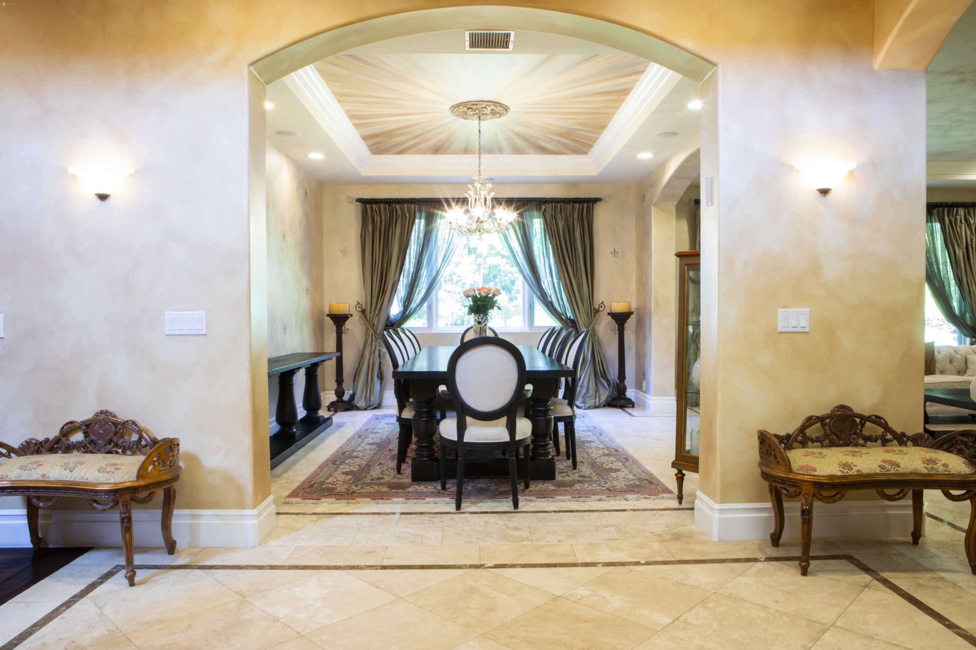 An interior space with a dining area featuring a black table and elegant chairs, framed by decorative walls and a chandelier.