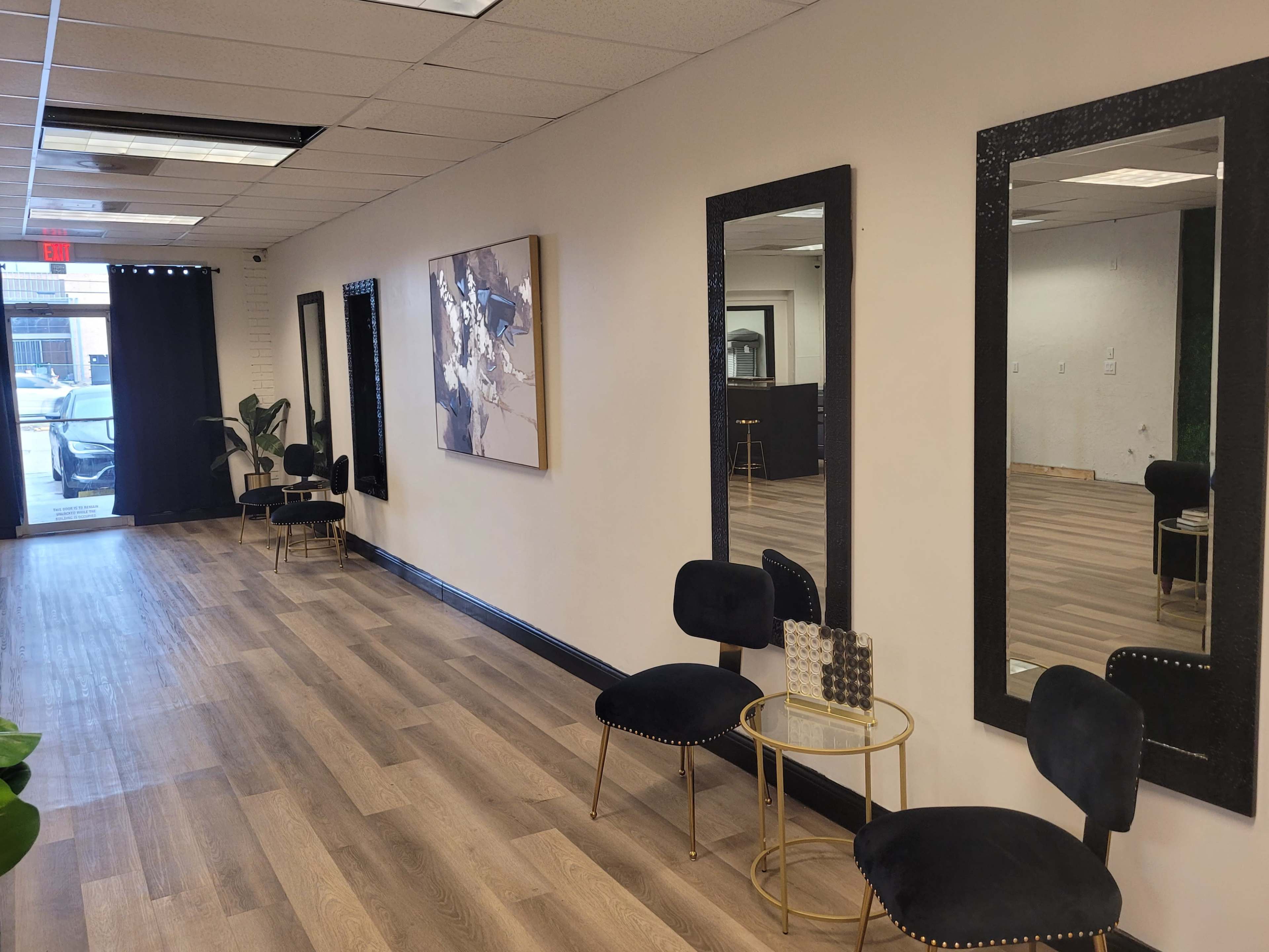A well-lit hallway features two large mirrors, modern chairs, and a piece of abstract art on the wall.