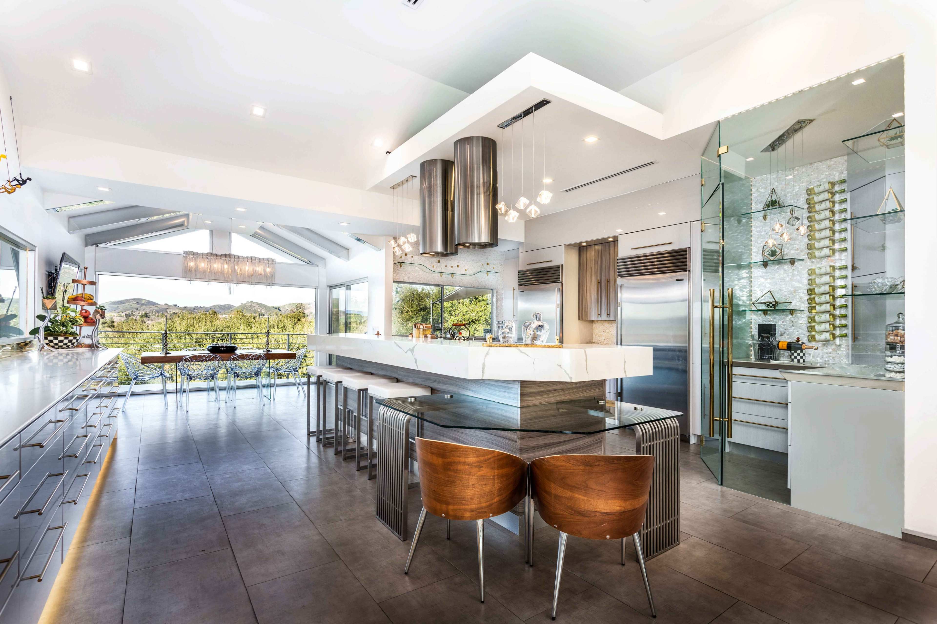A modern kitchen with sleek cabinetry, a large island, and panoramic windows overlooking a scenic outdoor landscape.