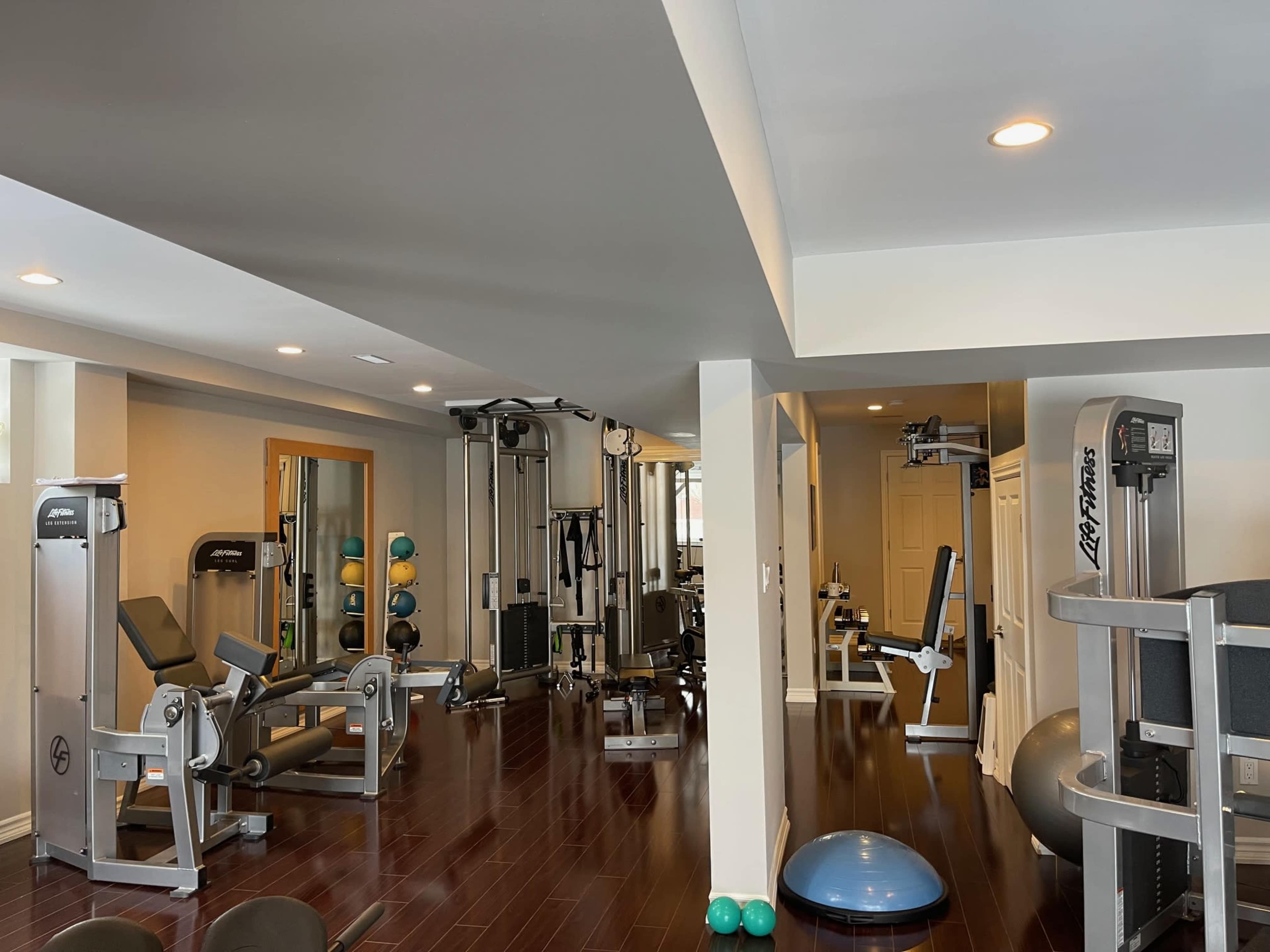 The image shows a spacious home gym equipped with various exercise machines, weights, and workout accessories.