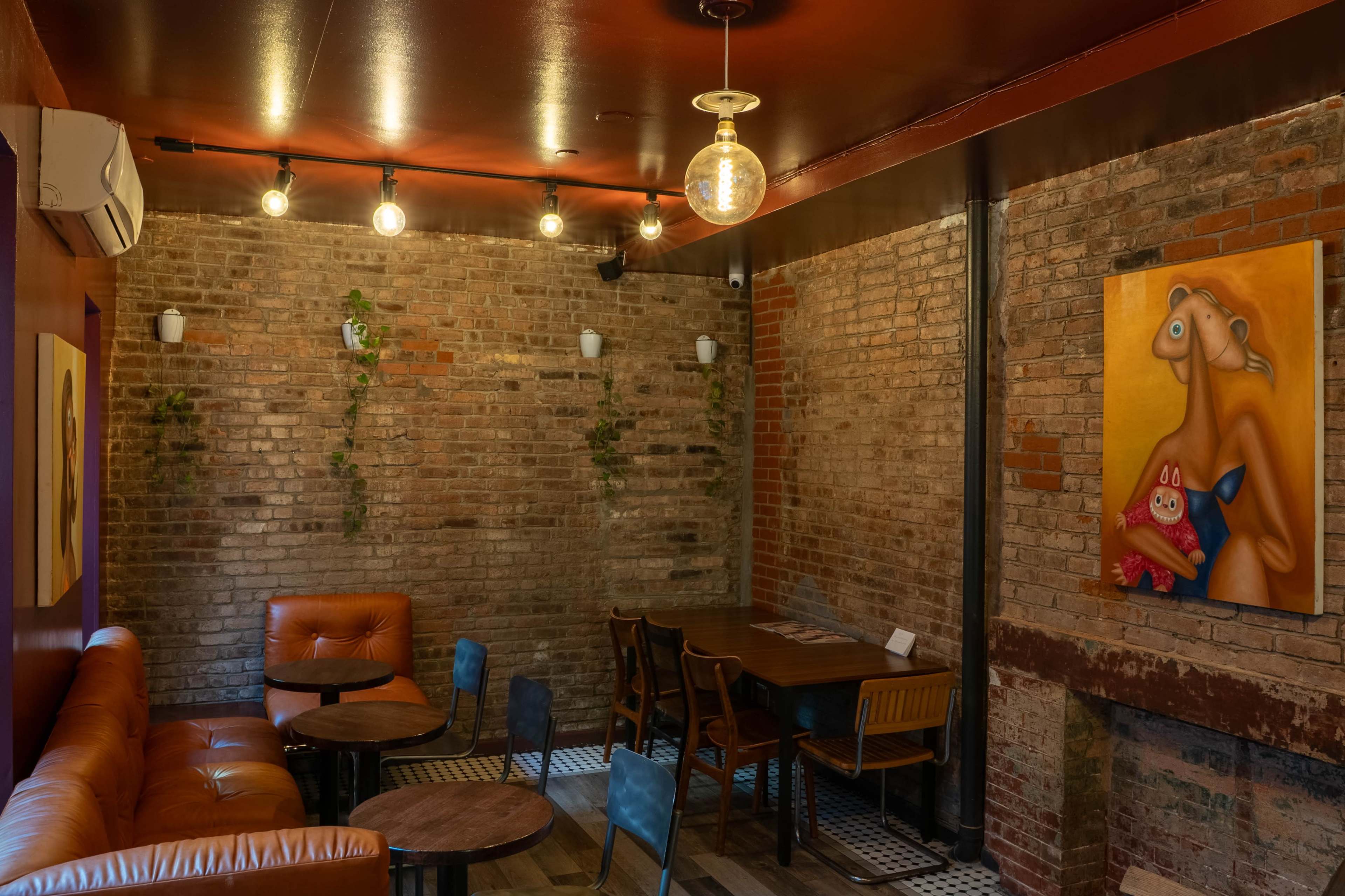 The image shows a cozy, modern café interior featuring exposed brick walls, wooden furniture, and artwork hanging on the walls.