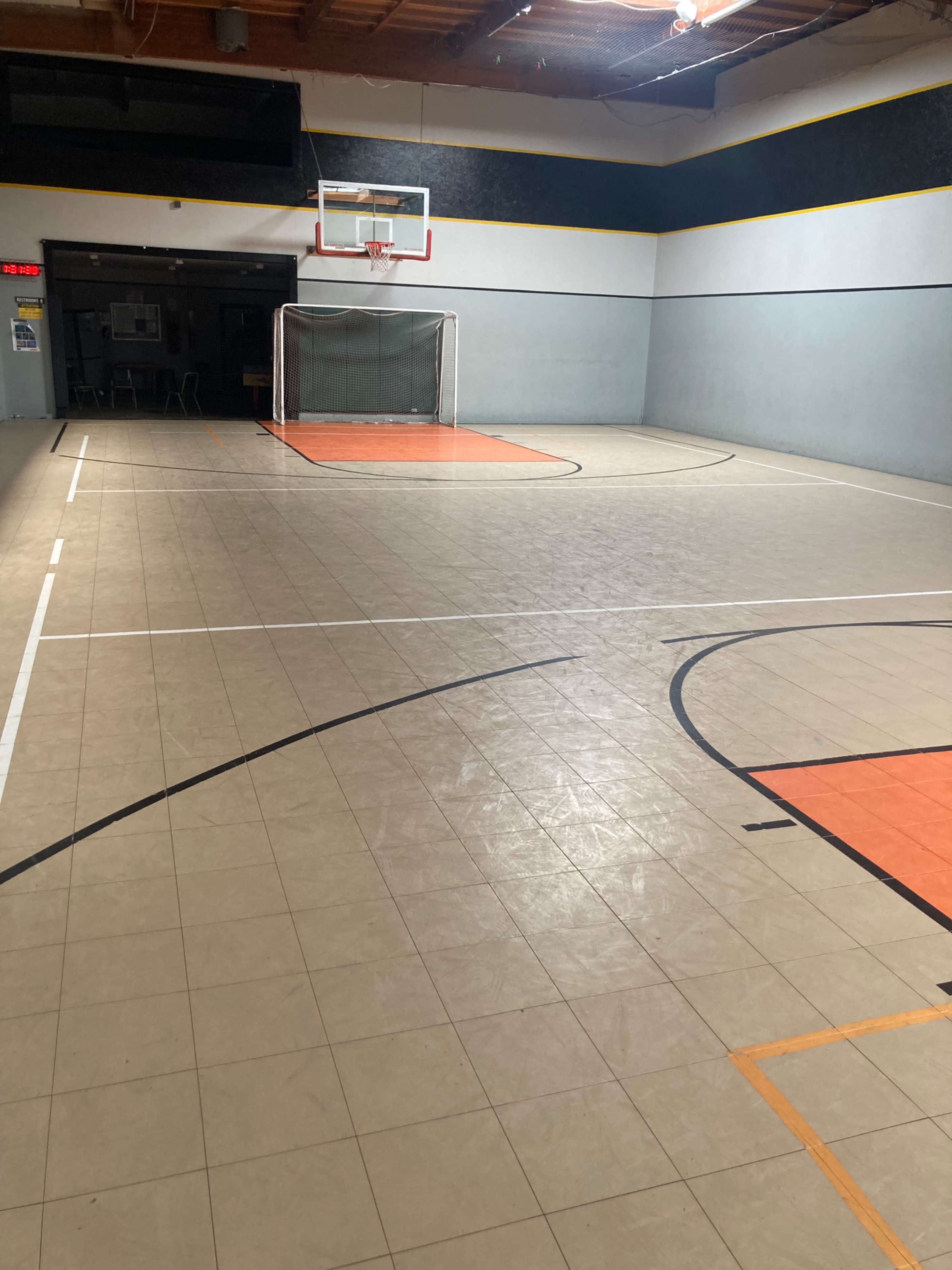 The image shows an indoor basketball court with a hoop at one end and a soccer goal at the opposite end, featuring an orange-painted area and marked boundaries.
