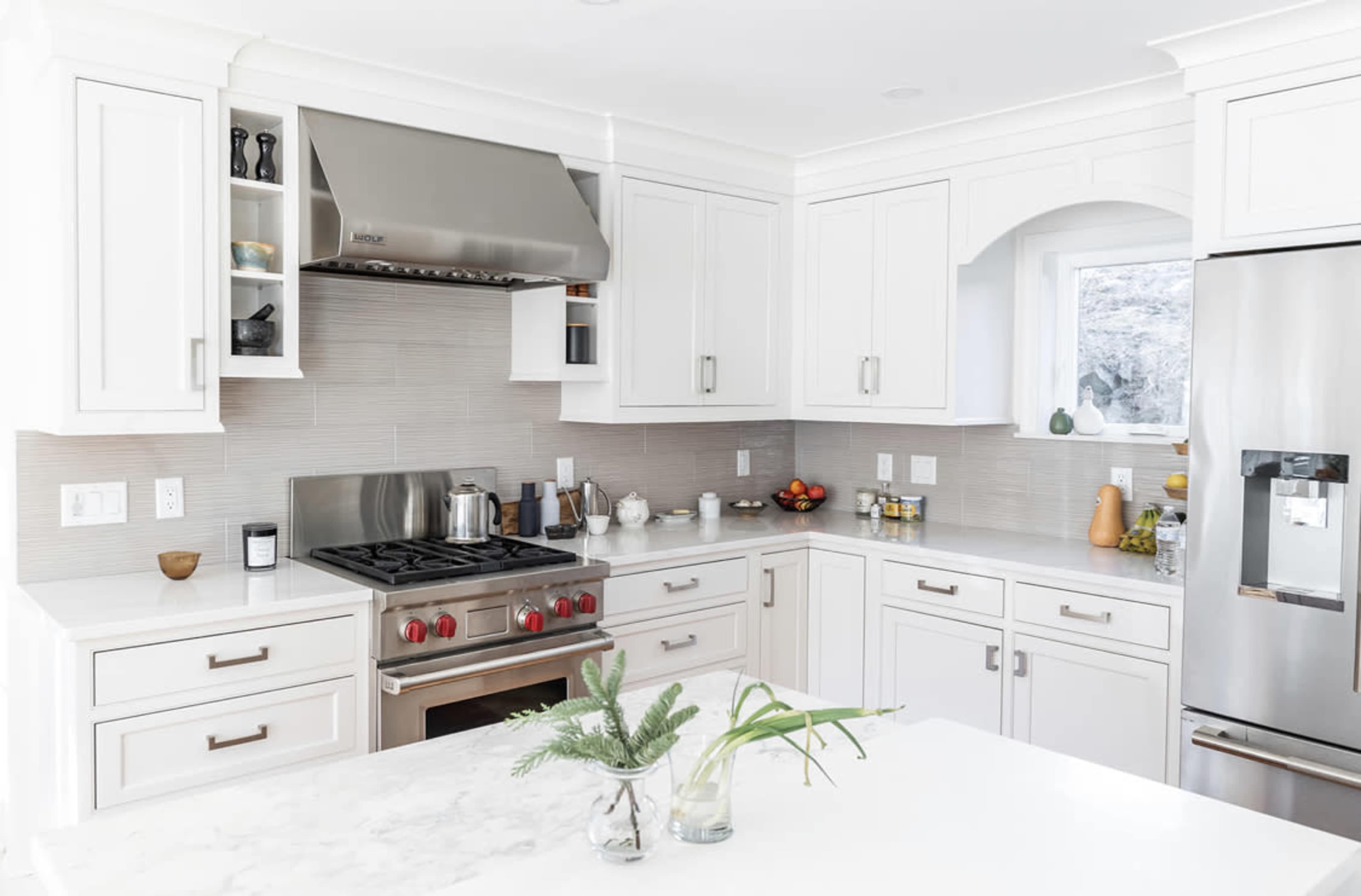 A modern kitchen features white cabinetry, a stainless steel refrigerator, and a gas stove beneath a metallic hood.
