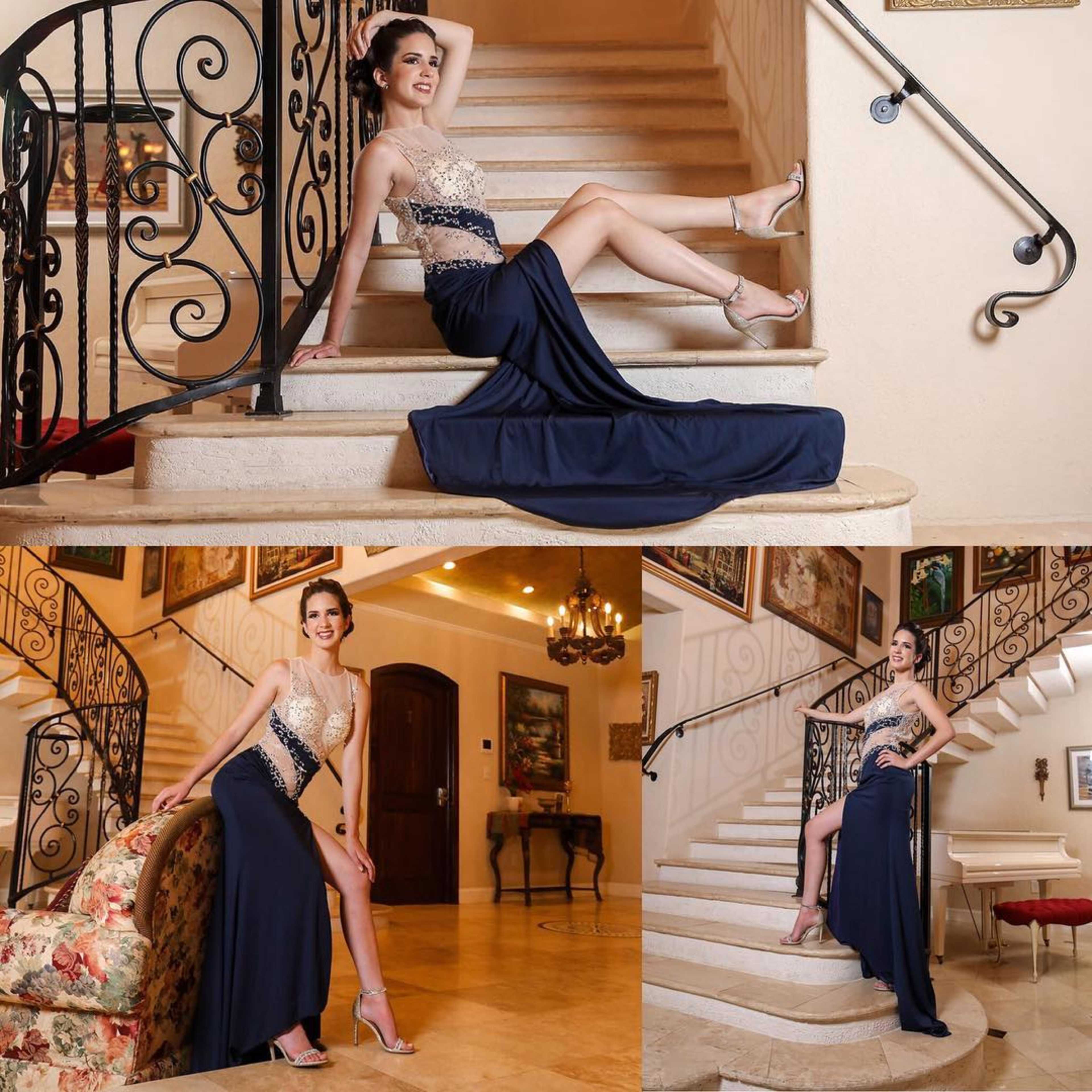 A woman in a formal navy dress poses on a staircase in a well-decorated interior.