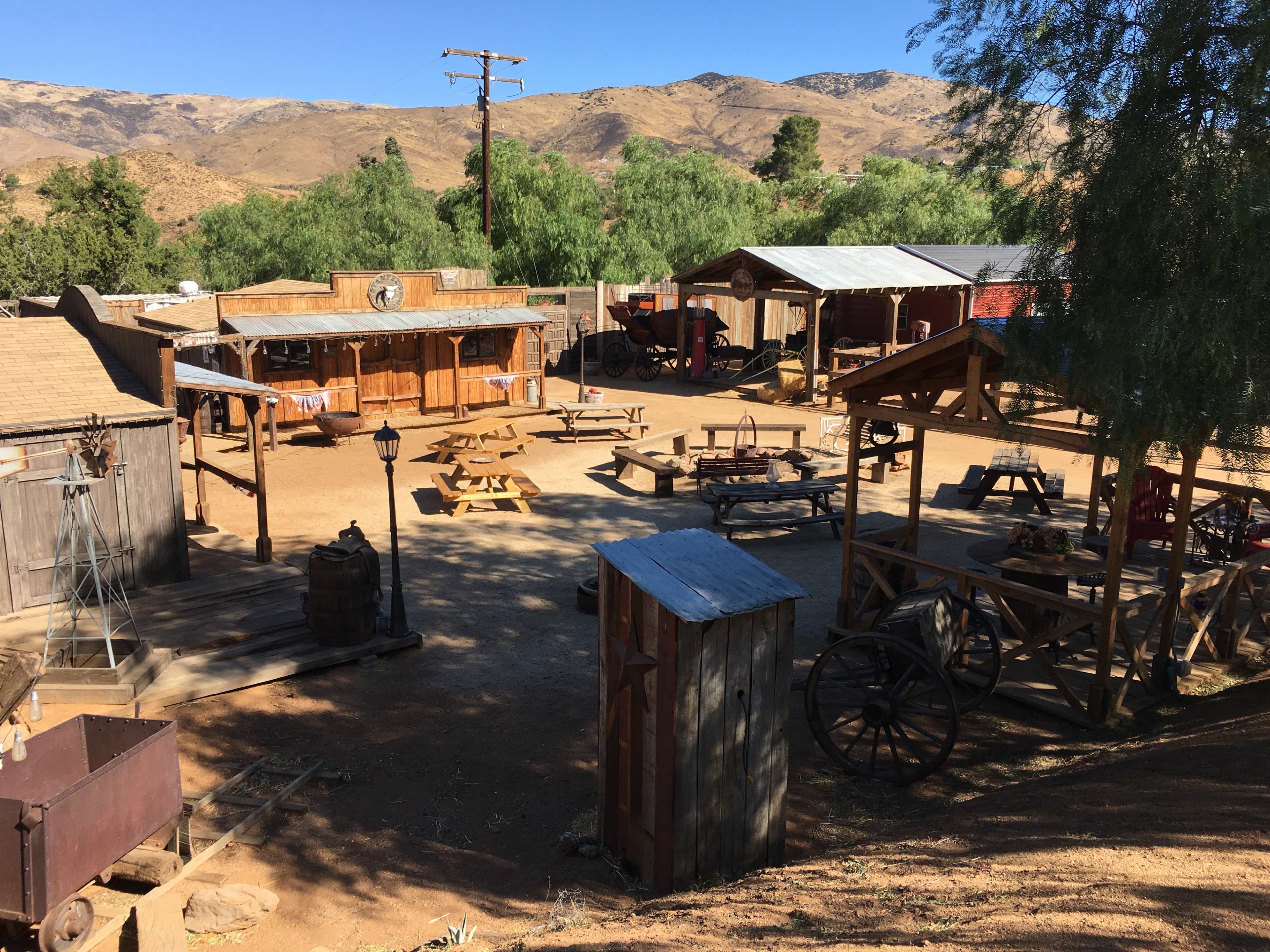 A rustic western-style movie set with wooden buildings, outdoor seating, and surrounding mountains.