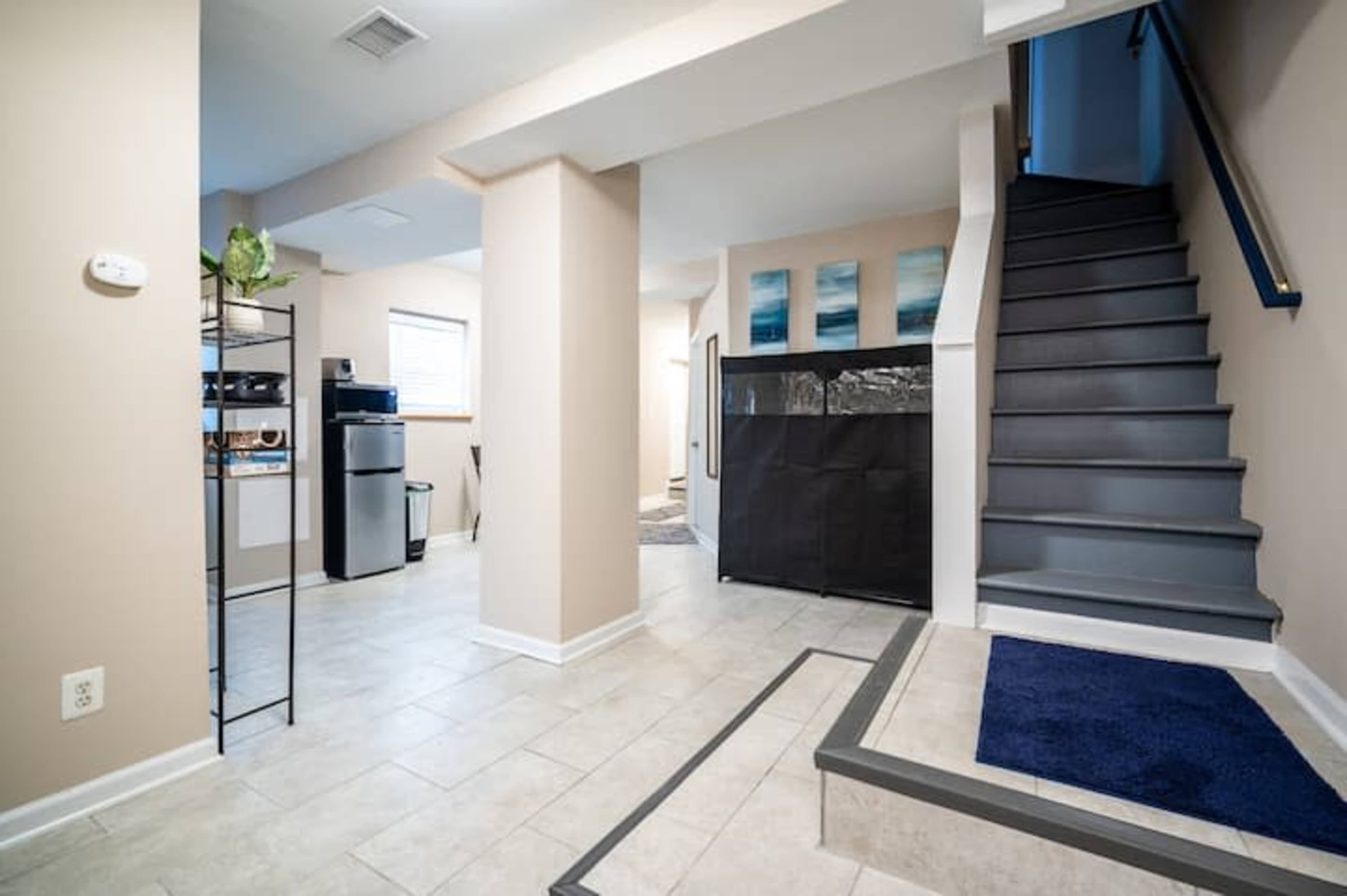 A well-lit entryway with a staircase on the right, a kitchenette area in the background, and a black storage unit near the center.