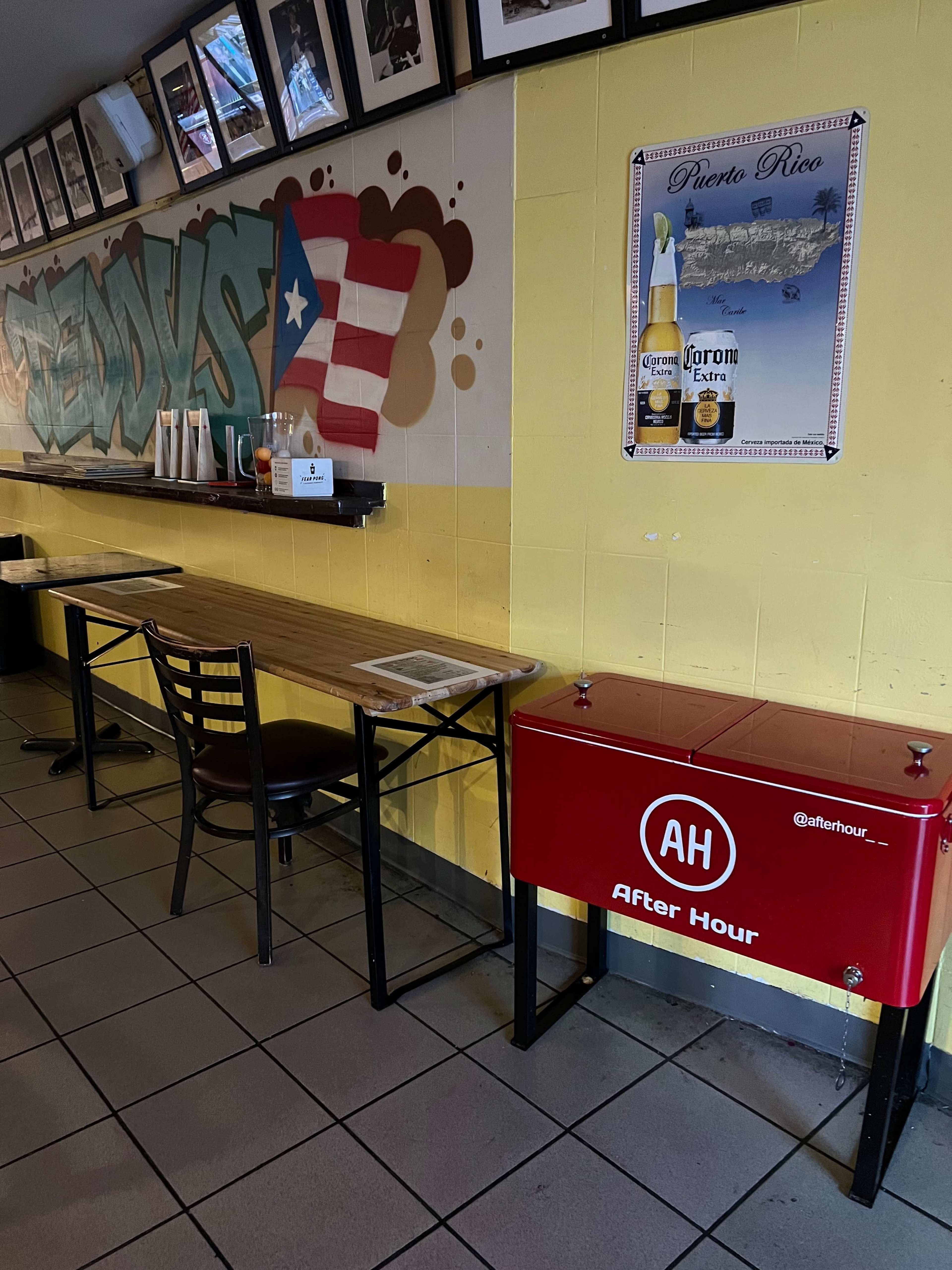 A brightly colored restaurant interior with a table and chairs along a wall adorned with a mural and framed photographs.