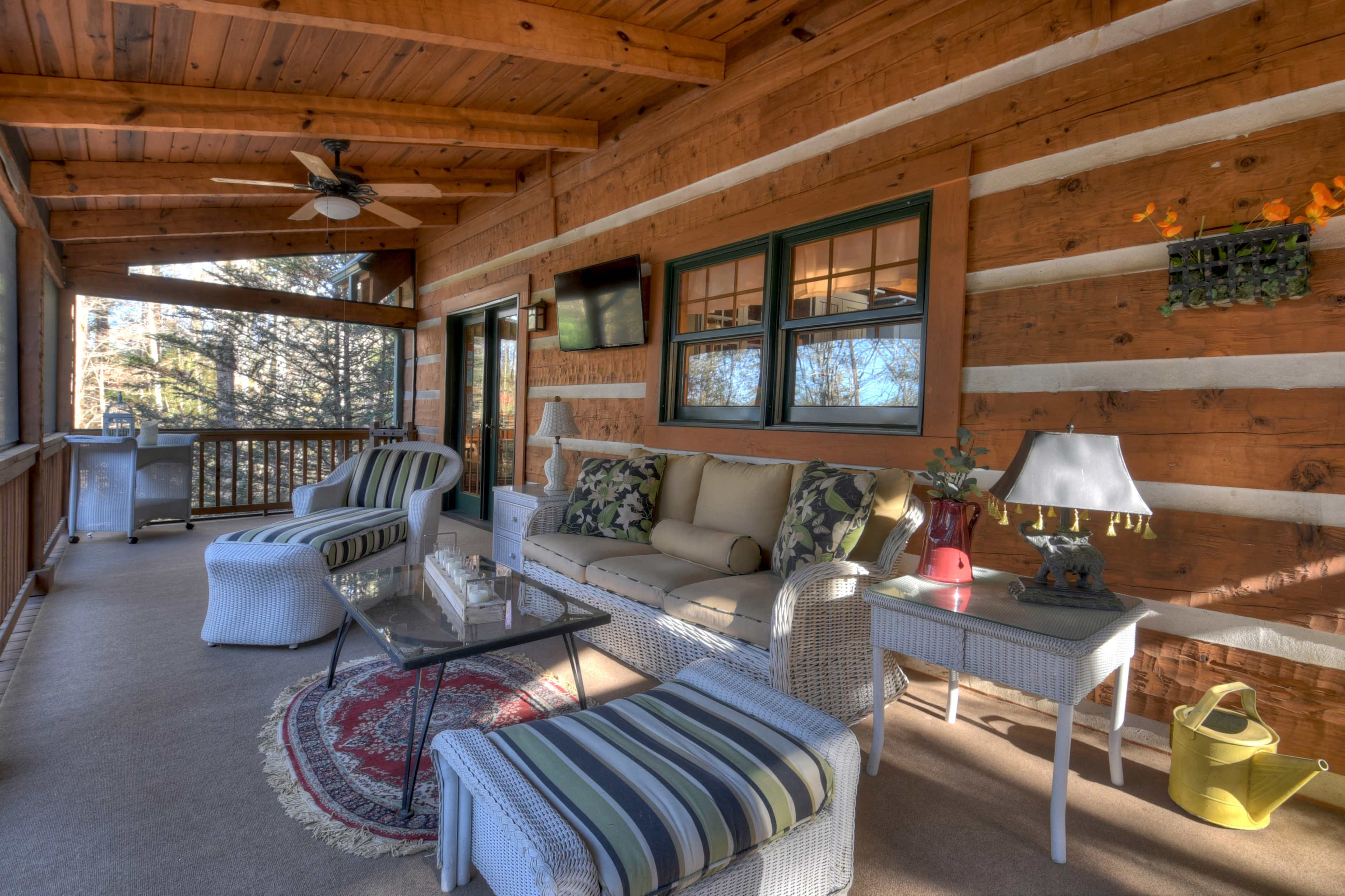 A rustic porch decorated with wooden panels, featuring comfortable seating, a glass coffee table, and various decorative elements.