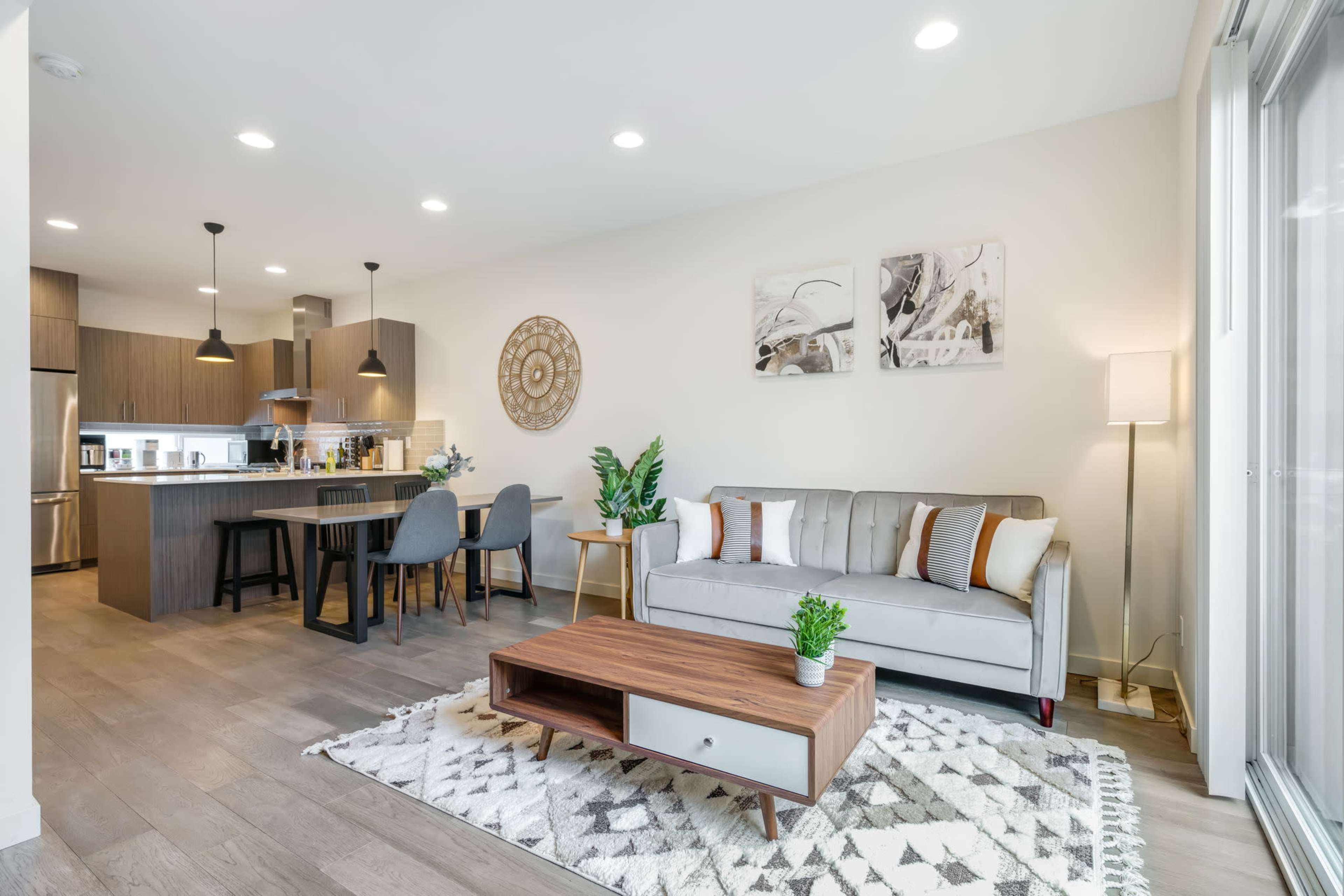 A modern open-concept living space with a dining area, kitchen, and a seating area featuring a sofa and a coffee table on a patterned rug.