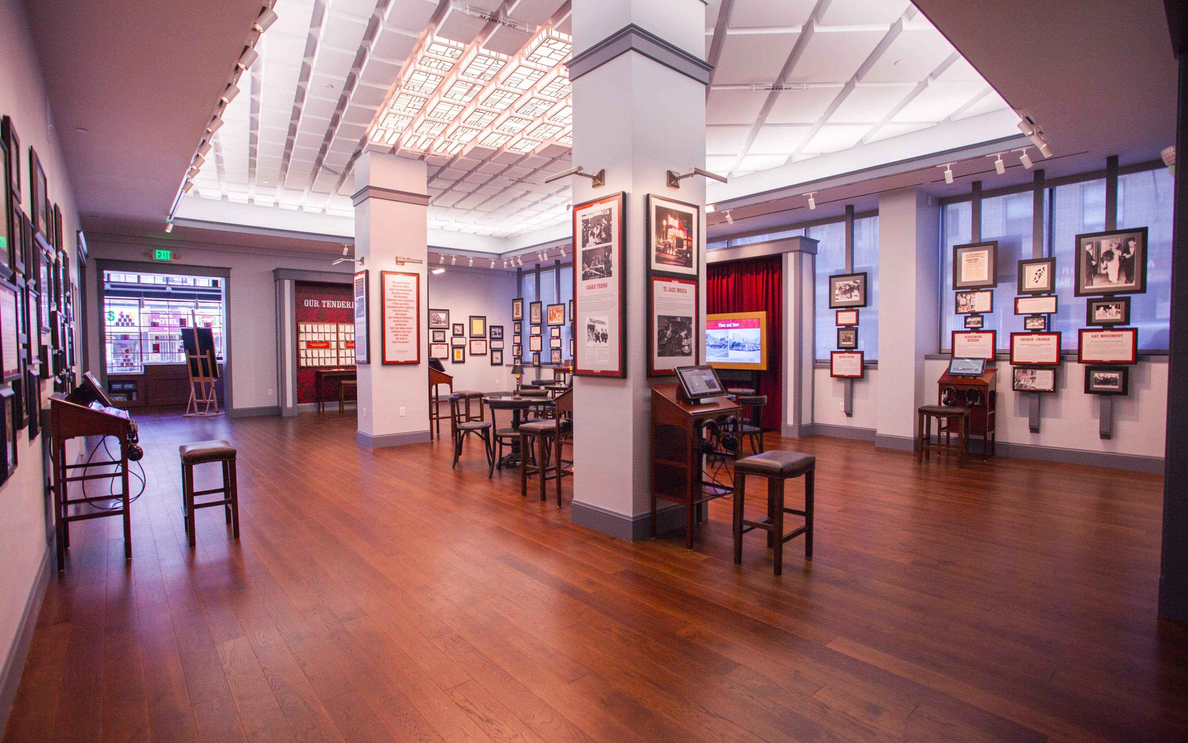 A spacious museum interior featuring wooden floors, framed photographs on the walls, and several tables and chairs arranged for visitors.
