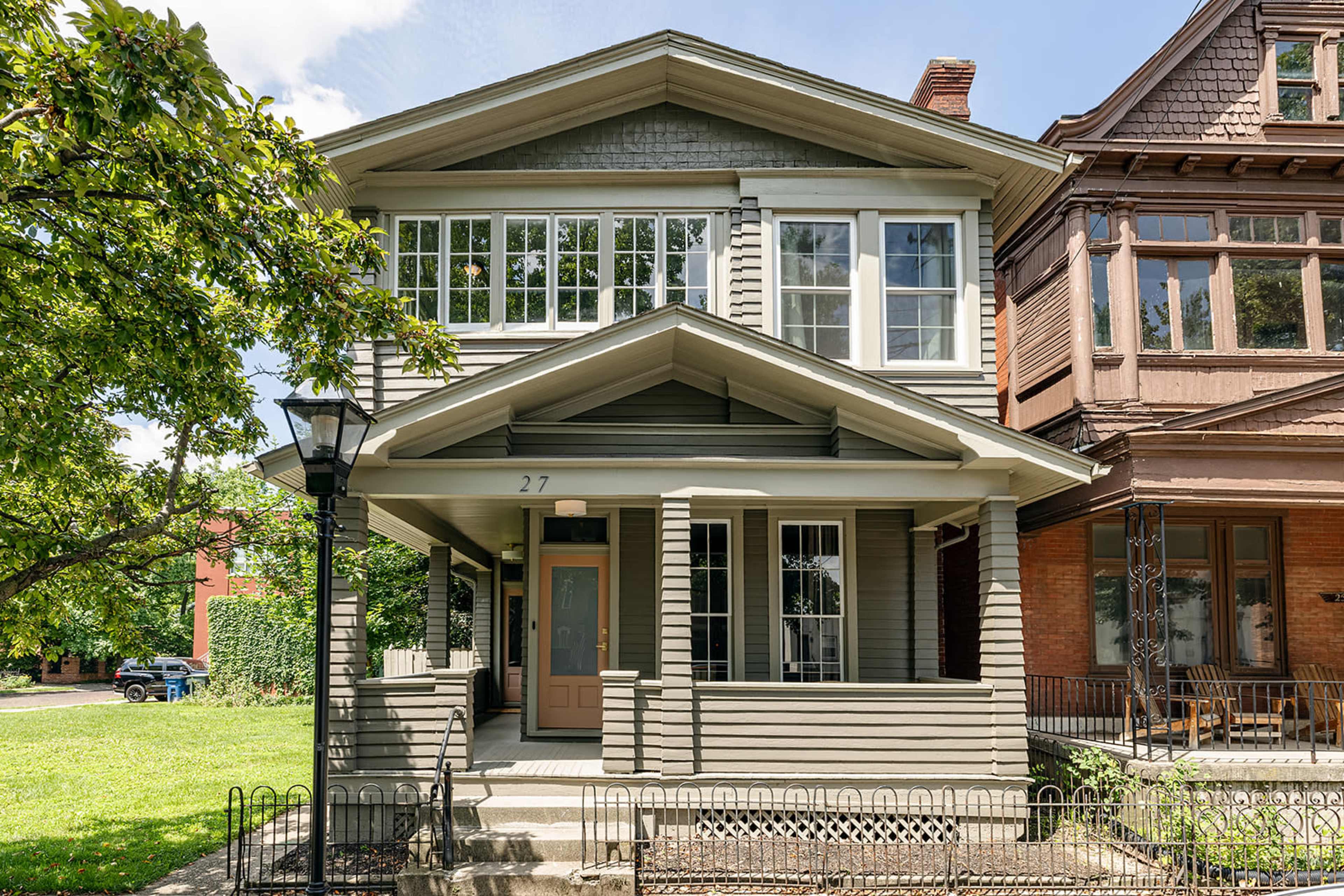 A two-story gray house with multiple windows and a front porch, situated next to a similarly styled building.