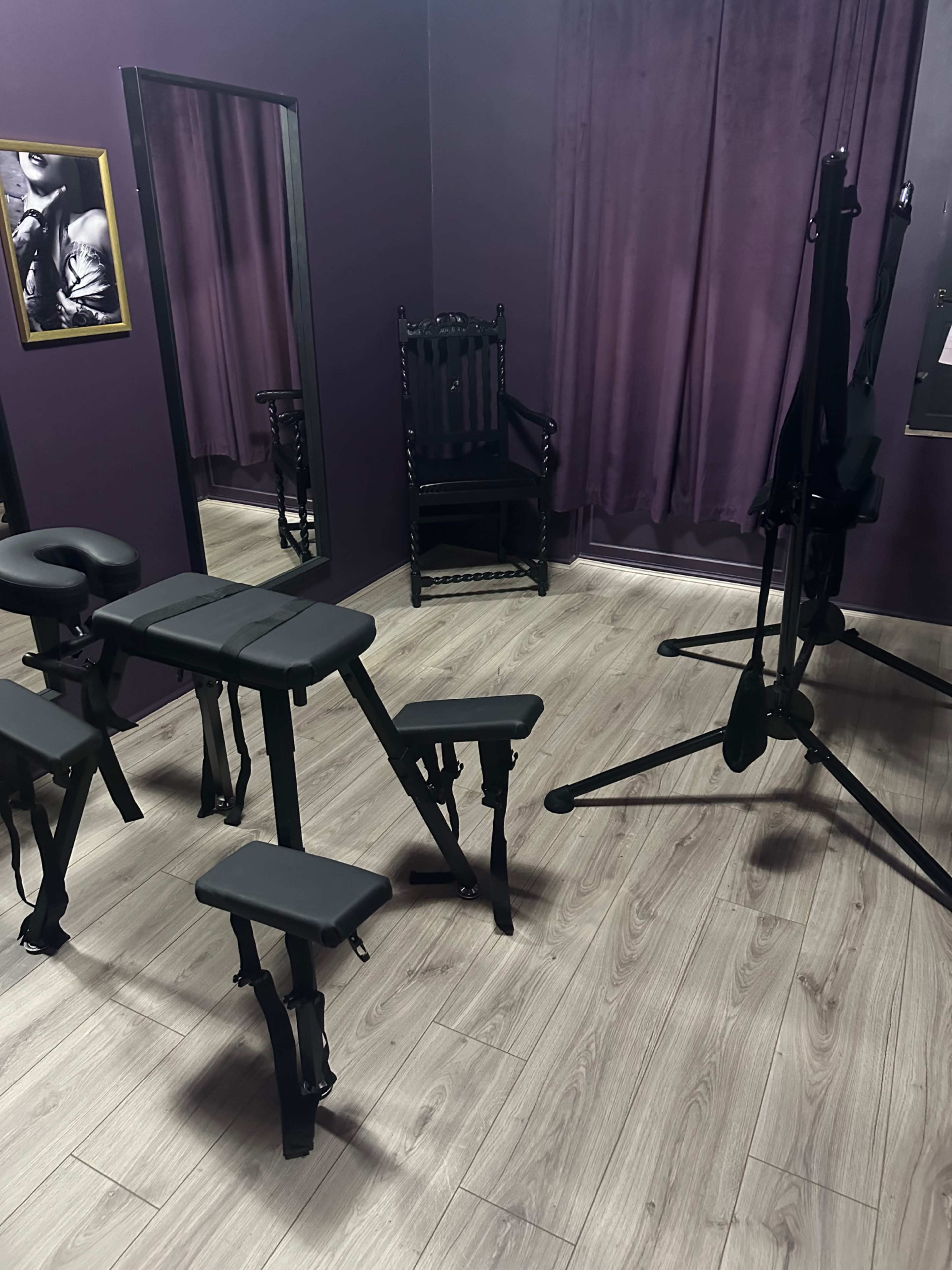 The image shows a small room with purple walls, featuring a black mirror, a chair, and several adjustable stools arranged near a stand.