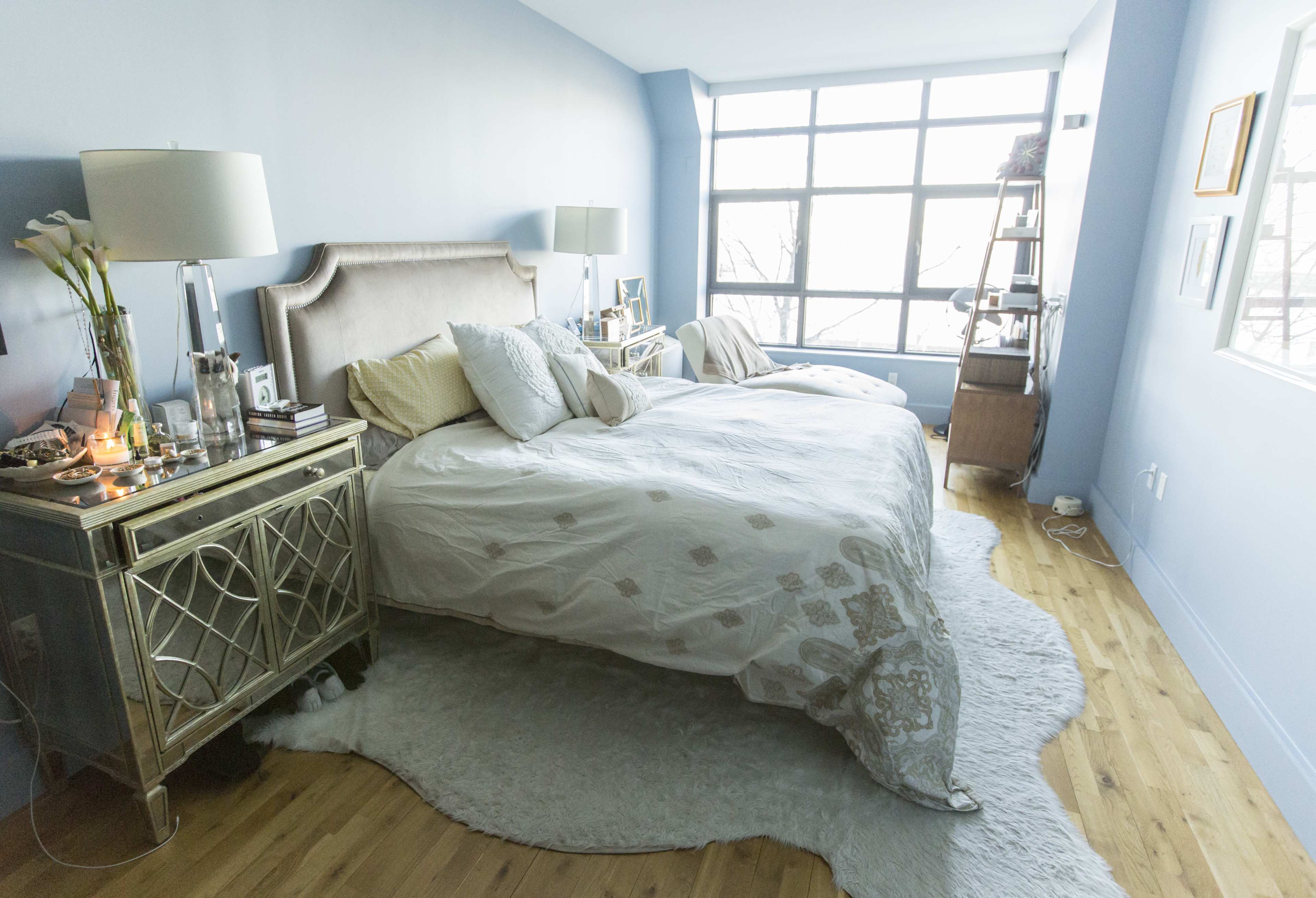 The bedroom features a light blue wall, two beds with white bedding, a decorative rug, and a window providing natural light.