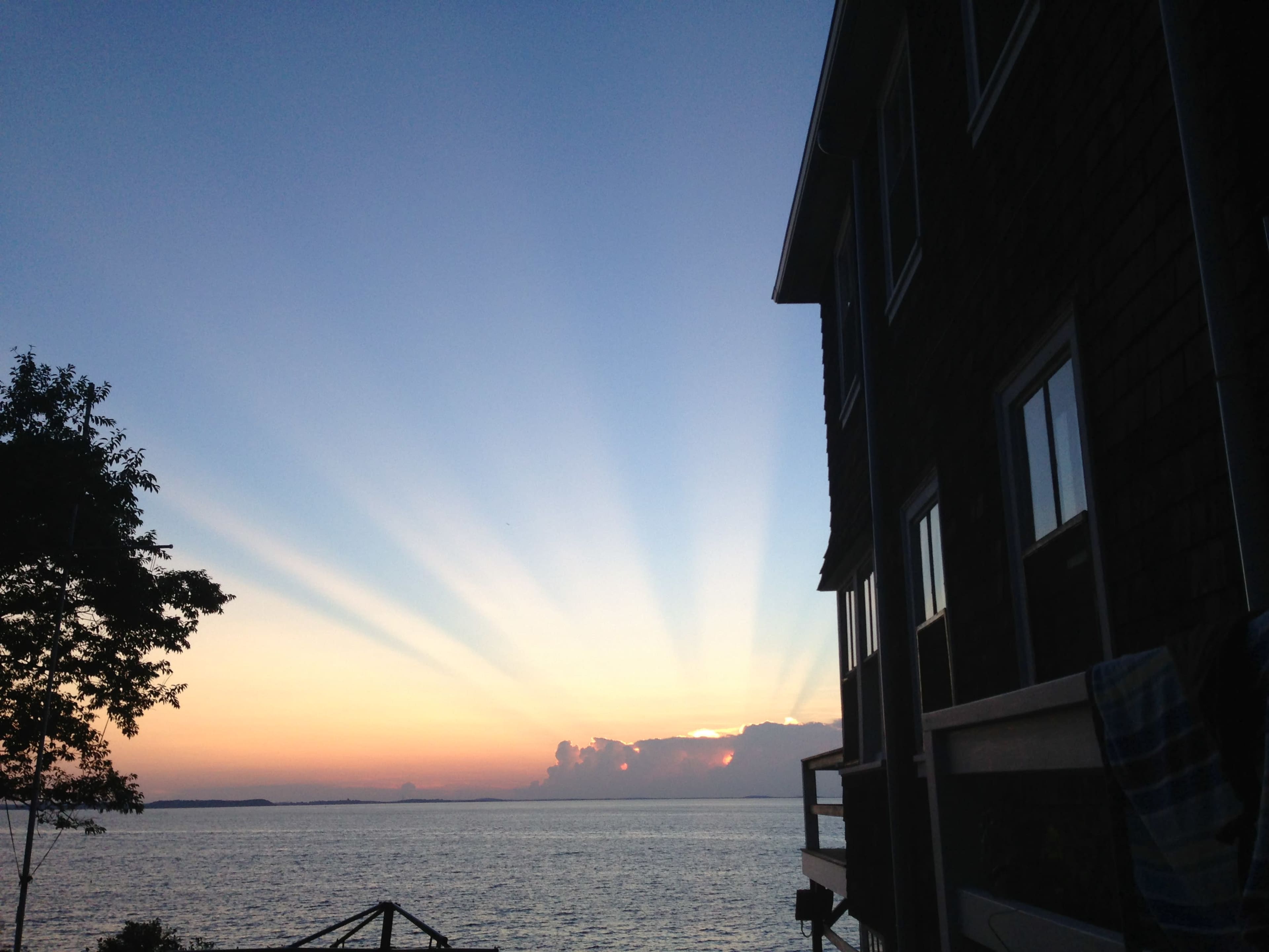 A sunset over the water, with rays of light extending from the horizon and a building visible on the right side.