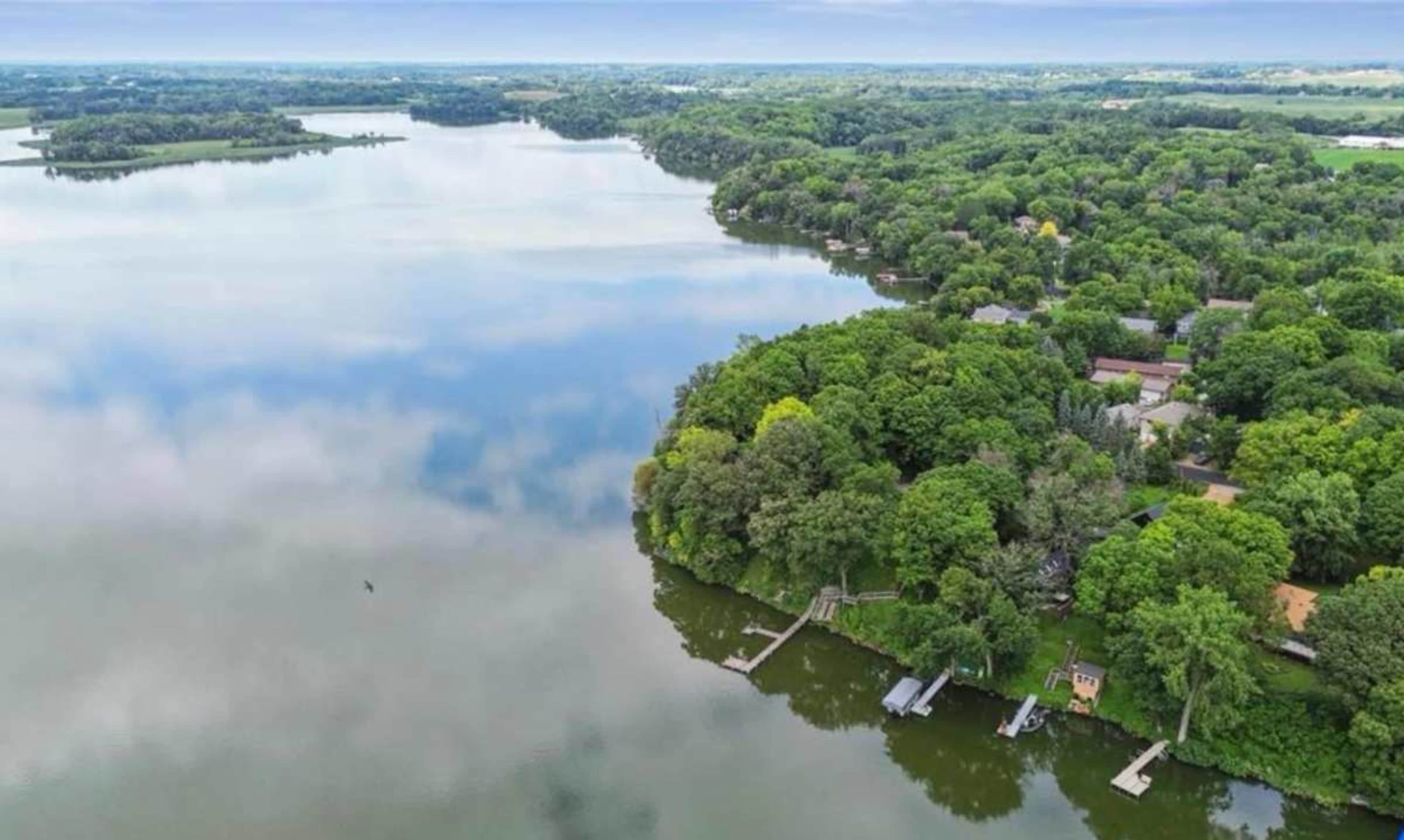 The image shows a serene lake bordered by lush greenery and residential properties.