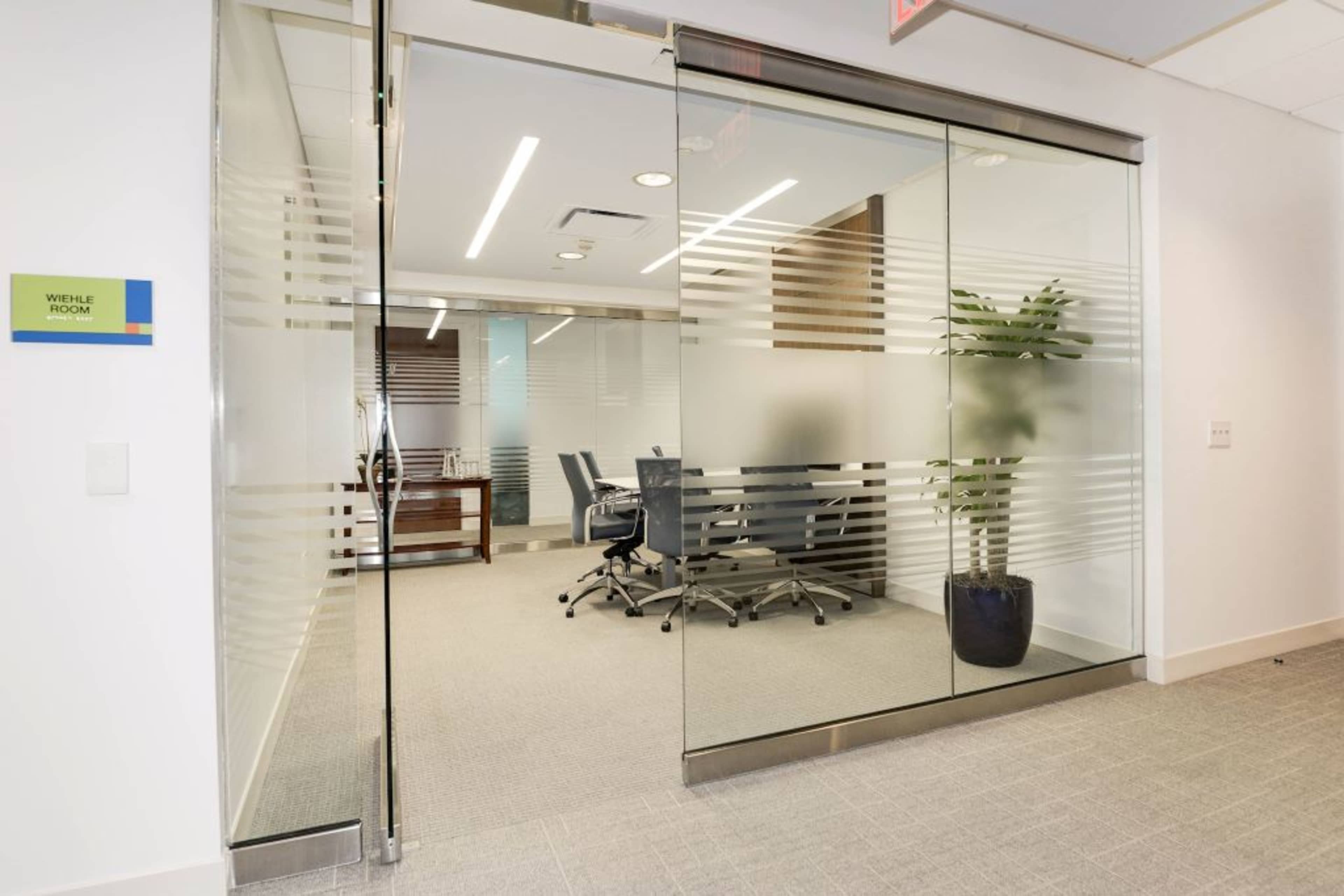 A modern conference room with glass sliding doors, featuring a table and chairs, and a nearby decorative plant.