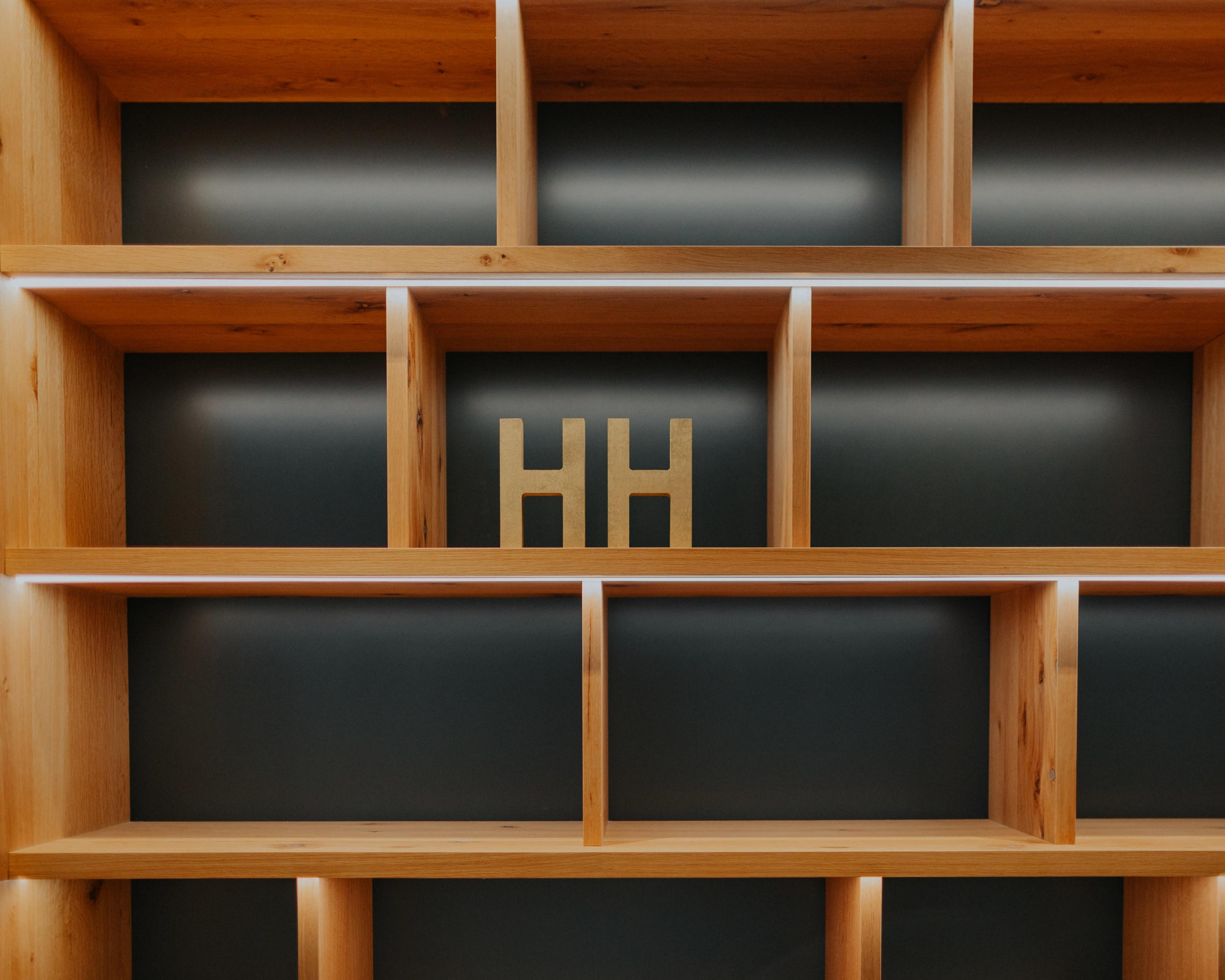 The image features a wooden shelving unit with several open compartments, displaying a pair of gold "HH" letters prominently in the center.